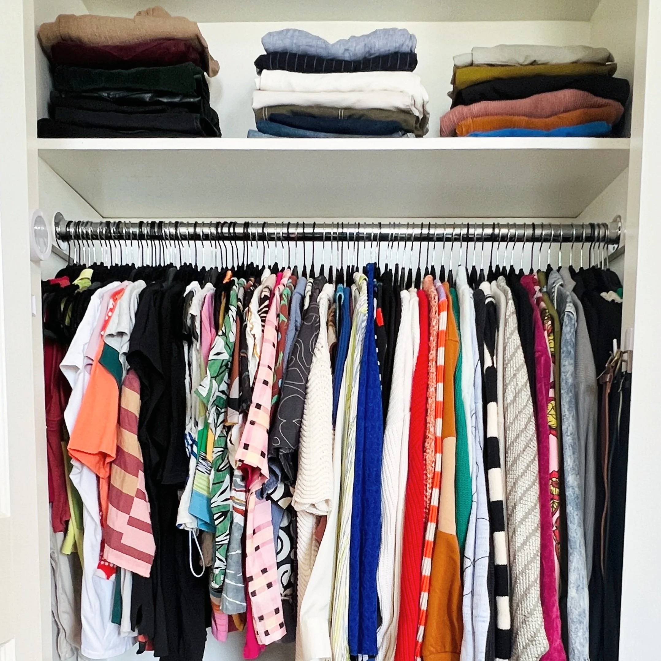 A photo from a closet organizing and stylist session shows an open closet with a clothing rod filled with colorful shirts and tops, and a top shelf stacked with folded pants and shirts.