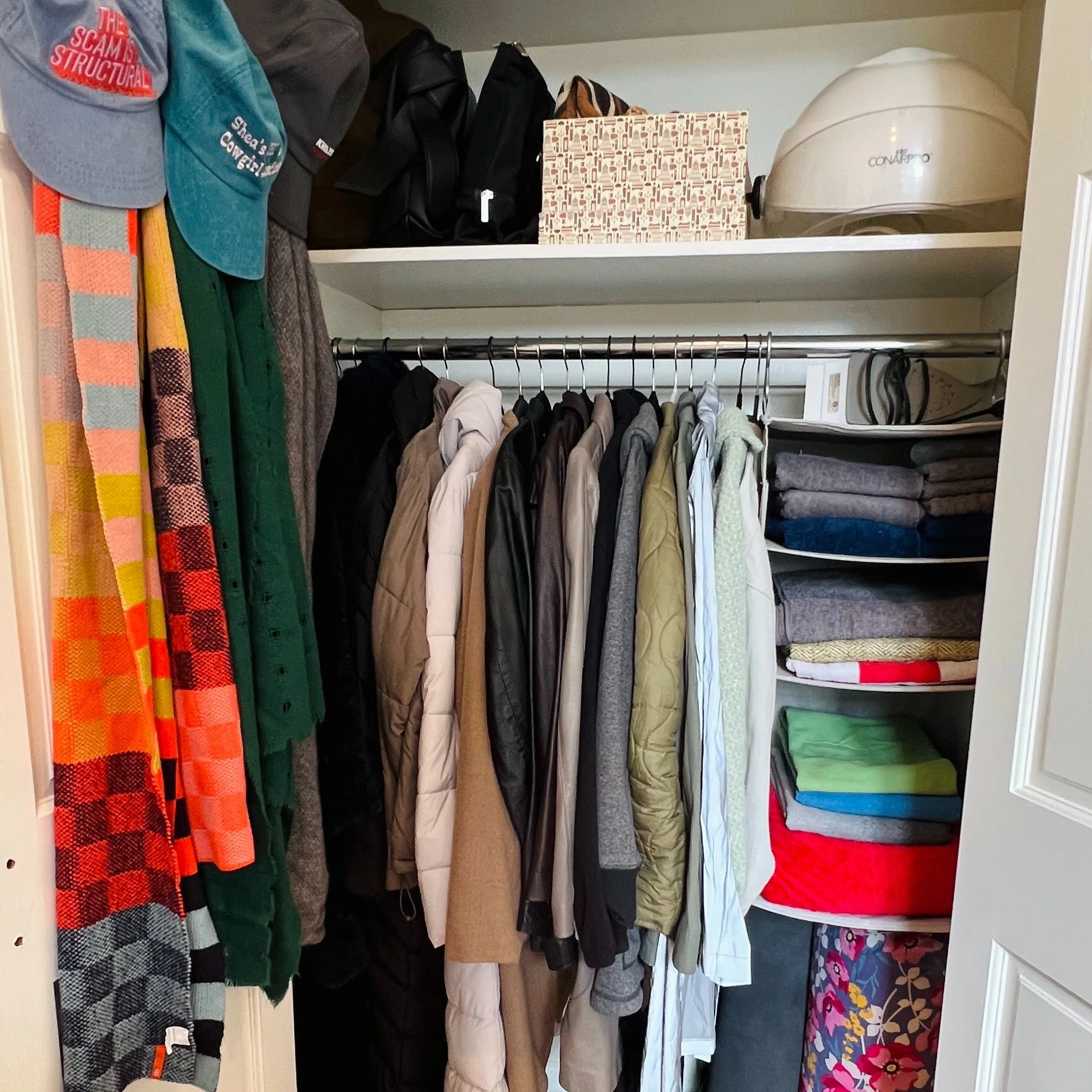 A photo from a closet organizing and stylist session shows an organized coat closet. On the left, there are hats and scarves hanging. The right side of the closet has neatly folded towels and blankets on shelves.