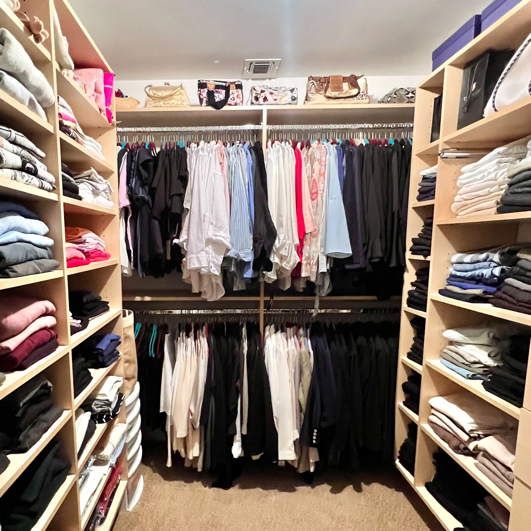 A photo from a closet organizing and stylist session shows an organized walk-in closet with shelves full of folded clothes on both sides and hanging shirts and pants in the middle.