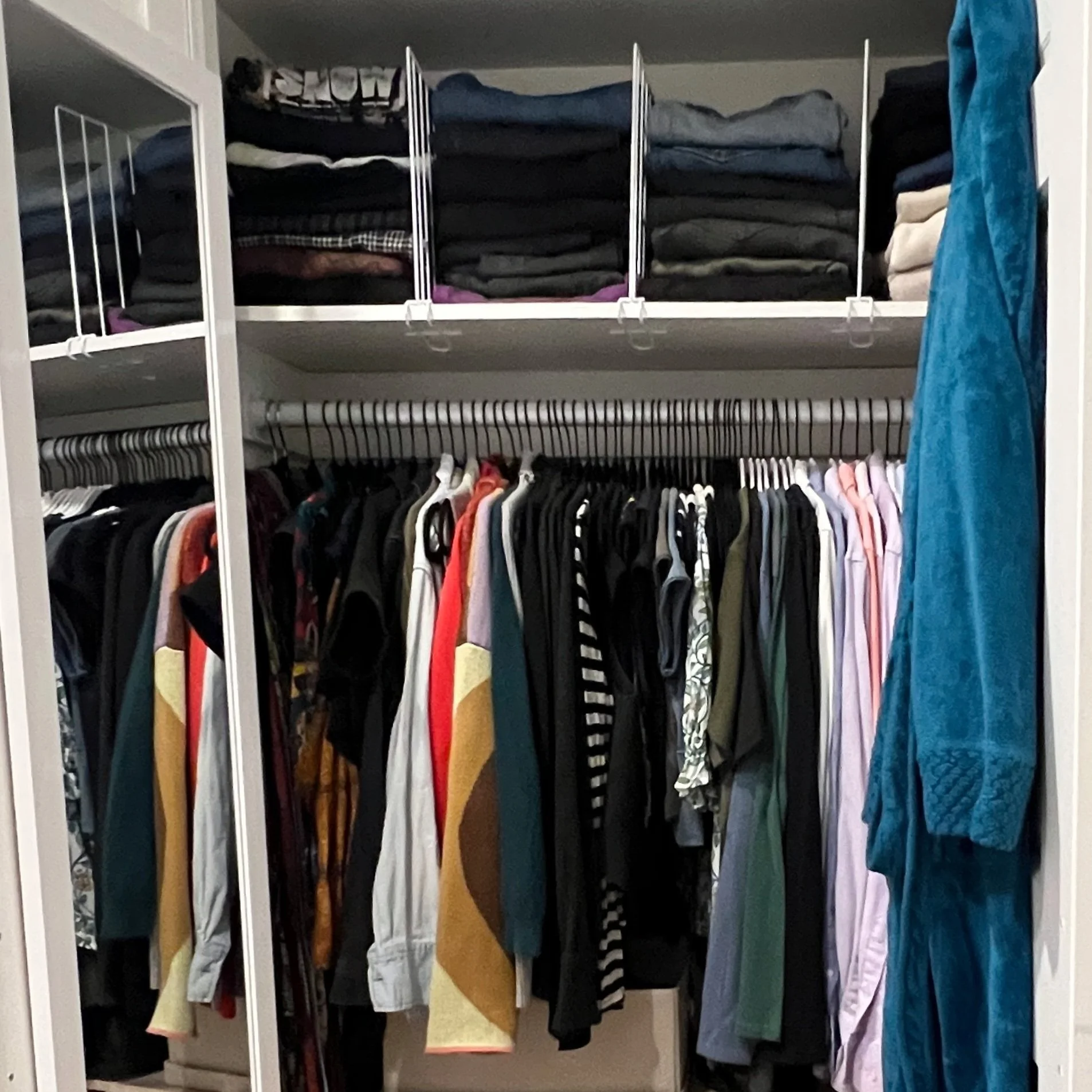 A photo from a closet organizing and stylist session shows the inside of a very tidy closet with clothes hanging on a rod and folded garments on shelves above.