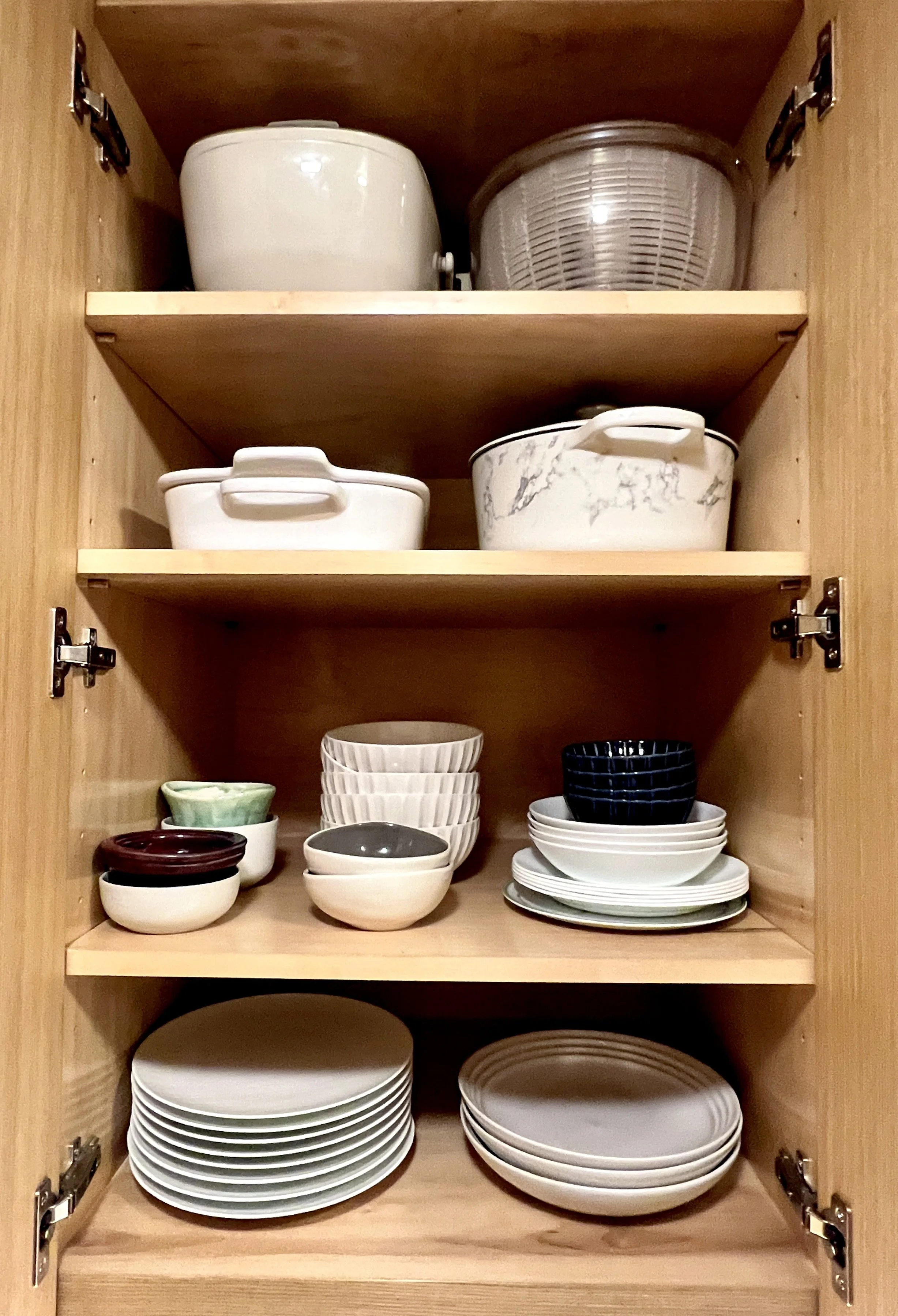 A photo from a home organizing session shows an open kitchen cabinet with neatly stacked dishes, bowls, and cookware.