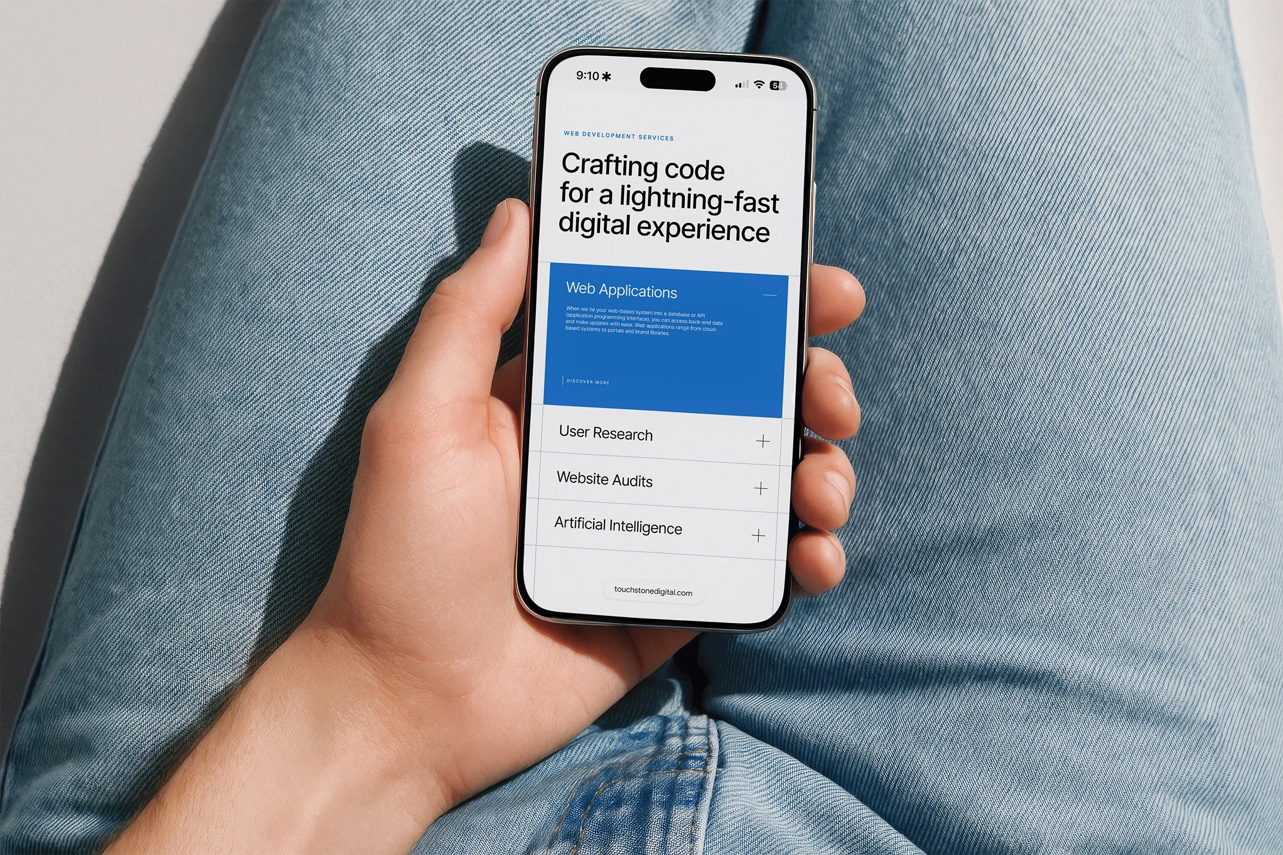 Close-up of a person holding a smartphone displaying a webpage about web development services, with a background of blue jeans.