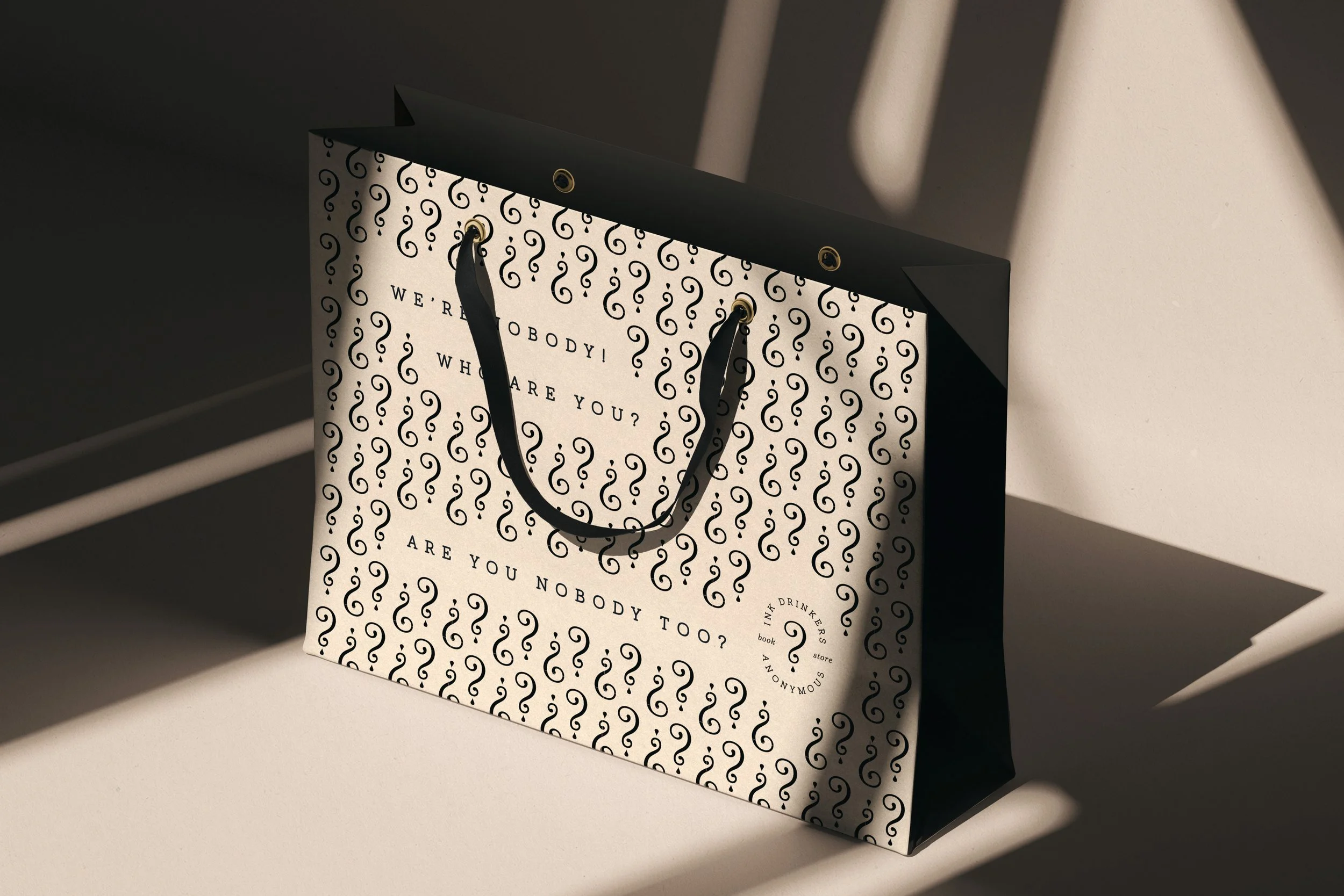 A black and white shopping bag with a decorative pattern and a message that reads, 'We resp. everybody! Who are you? Nobody too?'. The bag is placed on a white surface with shadows cast by a nearby window.