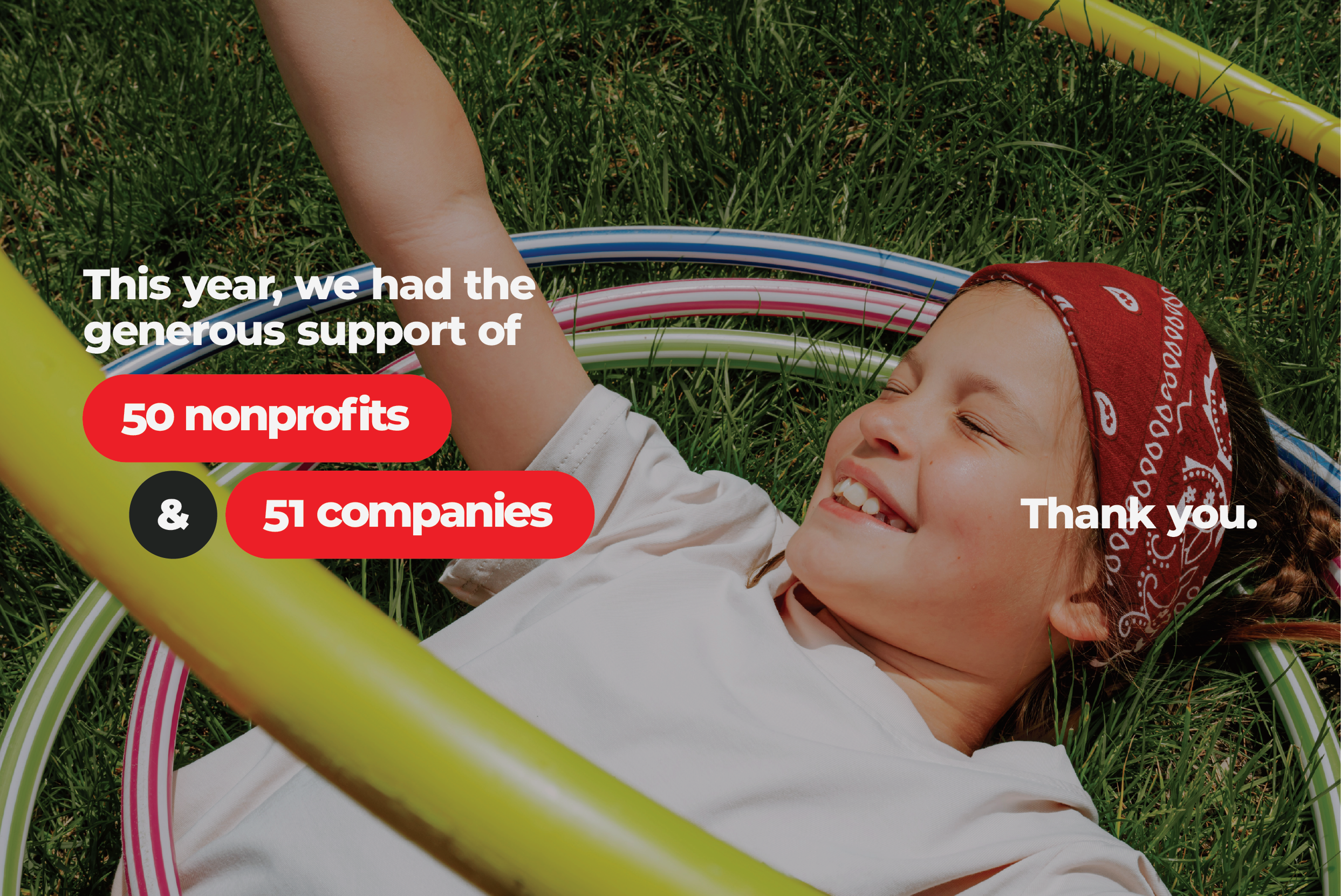 Child lying on grass, smiling, wearing a red bandana, white shirt, and surrounded by colorful hula hoops, with a message overlay expressing gratitude to nonprofits and companies.