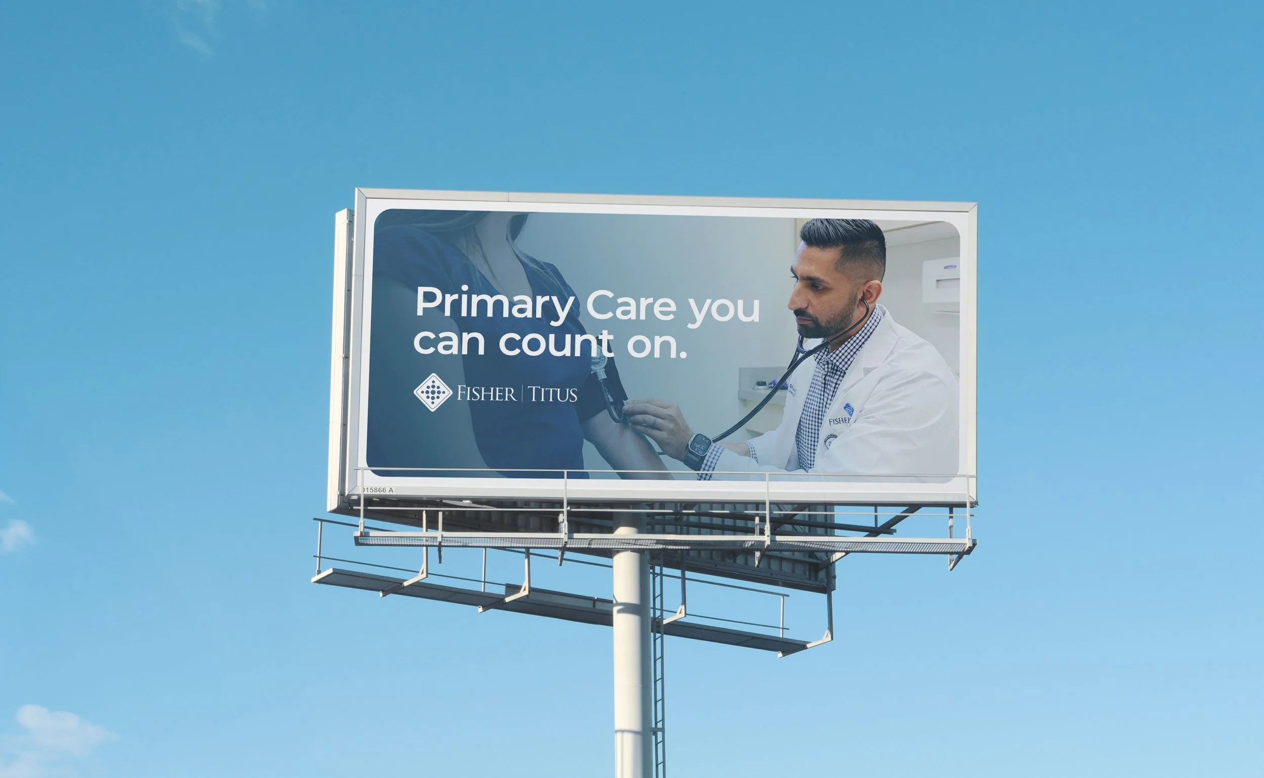 Billboard showing a male doctor using a stethoscope on a patient with a message about primary care and the Fisher Titus logo, set against a clear blue sky.