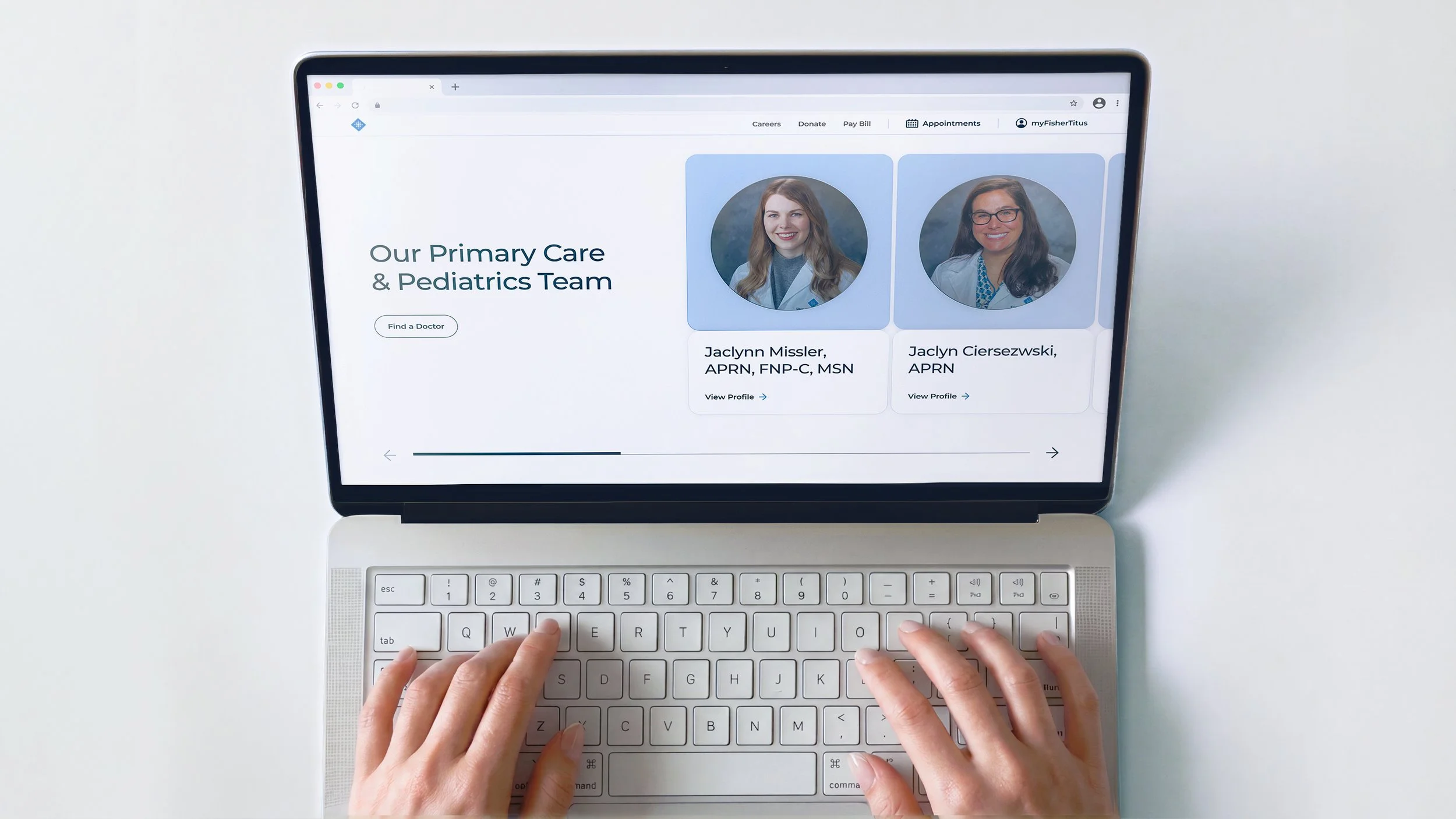 The image shows a person typing on a laptop keyboard displaying a healthcare website for primary care and pediatrics team, with profile photos of two female doctors on the screen.