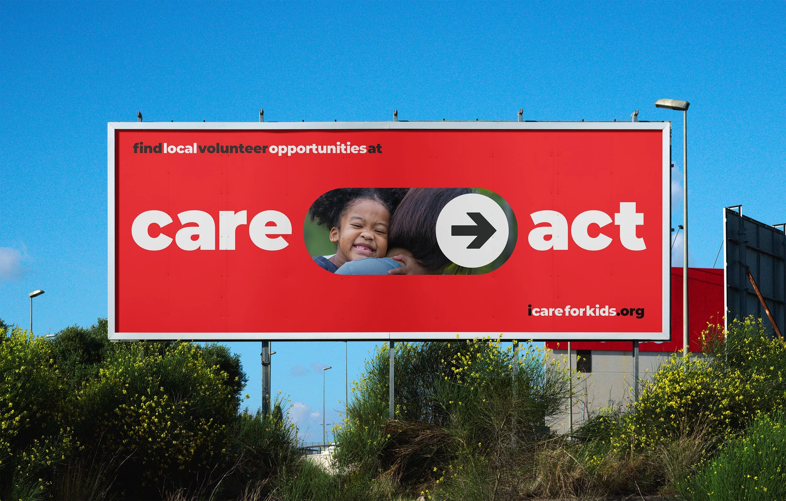 A large red billboard with the words "find local volunteer opportunities at care" on the left and an arrow pointing right, followed by the word "act" on the right. The billboard features a picture of a young girl hugging someone. The website address "icareforkids.org" appears in the bottom right corner. The billboard is outdoors against a blue sky with some green bushes and trees below.