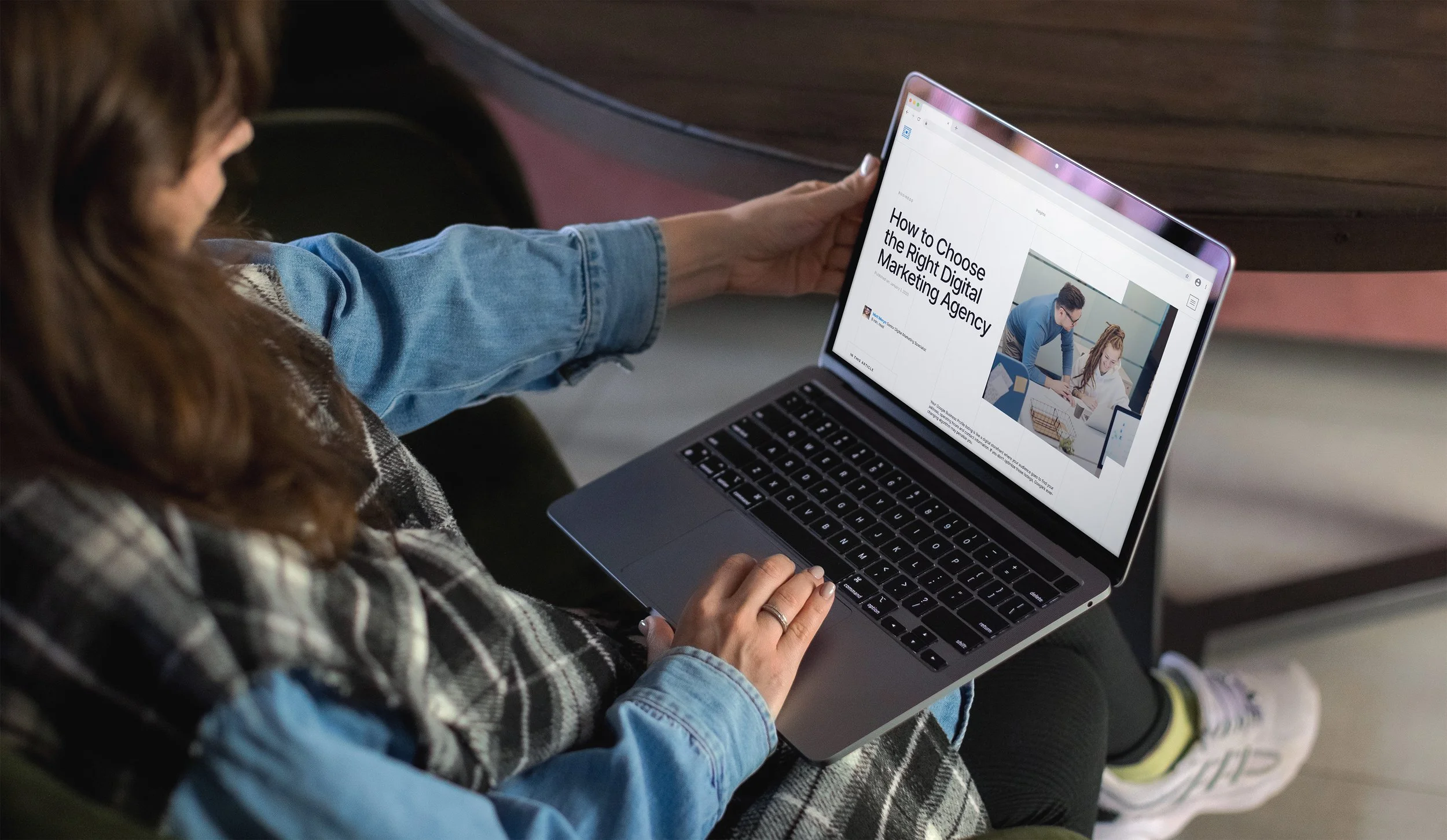 A person holding a laptop displaying an article titled 'How to Choose the Right Digital Marketing Agency' with a photo of two people working together in an office.