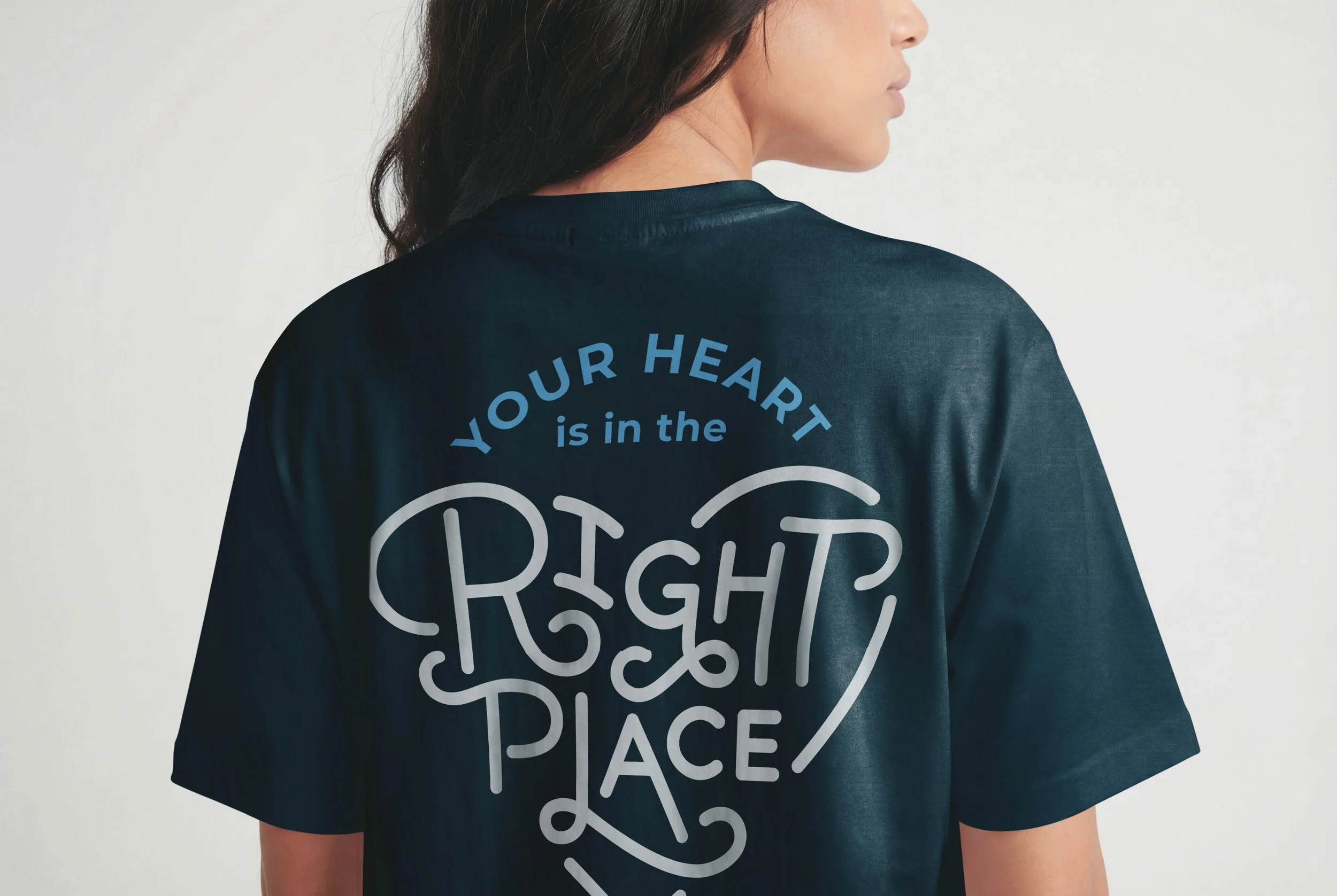 A person with dark hair wearing a black T-shirt with the phrase 'YOUR HEART is in the RIGHT PLACE' printed on the back.