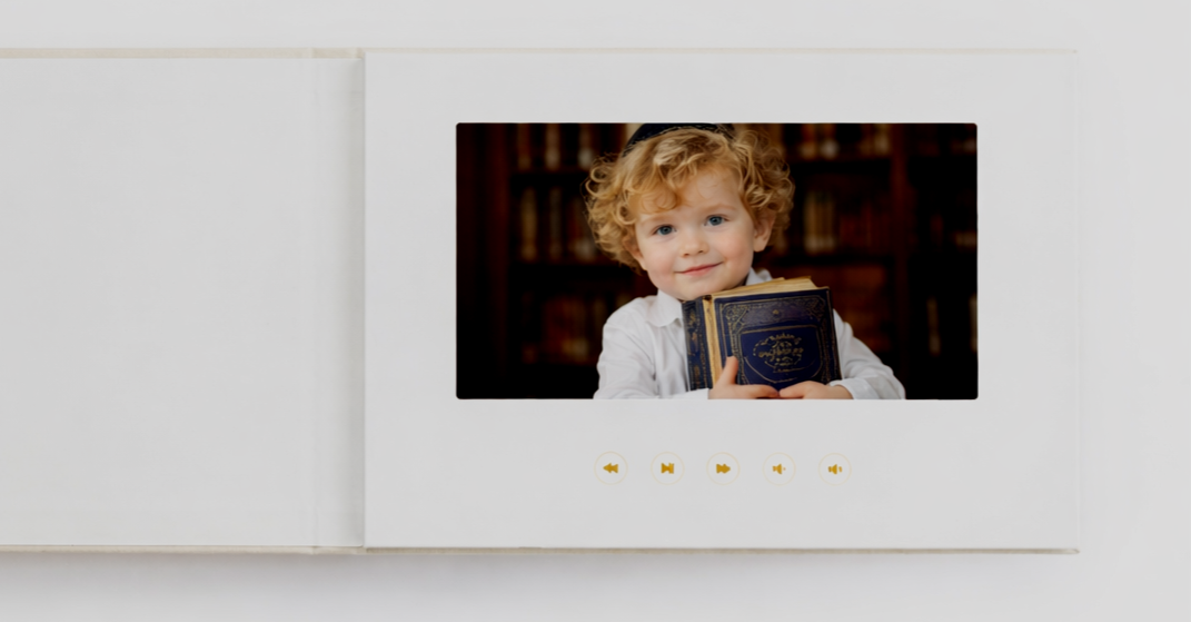 A young child with curly blonde hair holding a blue and gold book, smiling at the camera, inside a white box with media control buttons below.