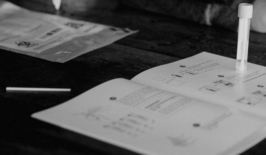 Open instruction manual or guidebook on a wooden surface with a test tube and a cotton swab.