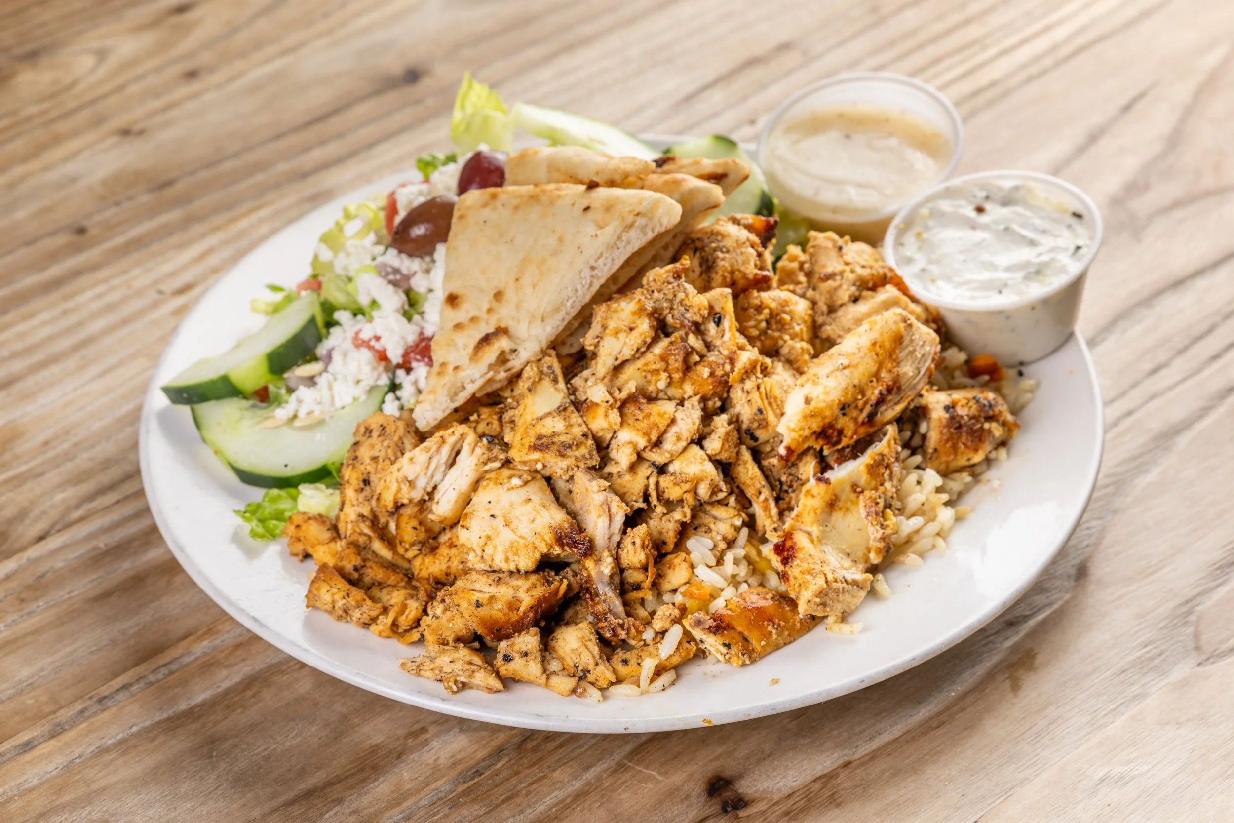 Platter of chicken gyro meat with rice, pita bread, Greek salad, and two cups of dipping sauces.
