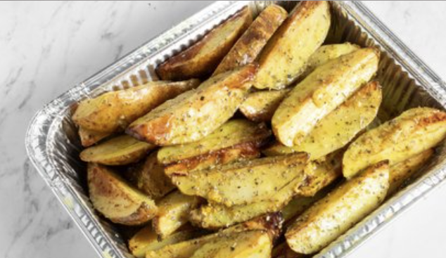 Baked potato wedges in a foil container on a white surface.