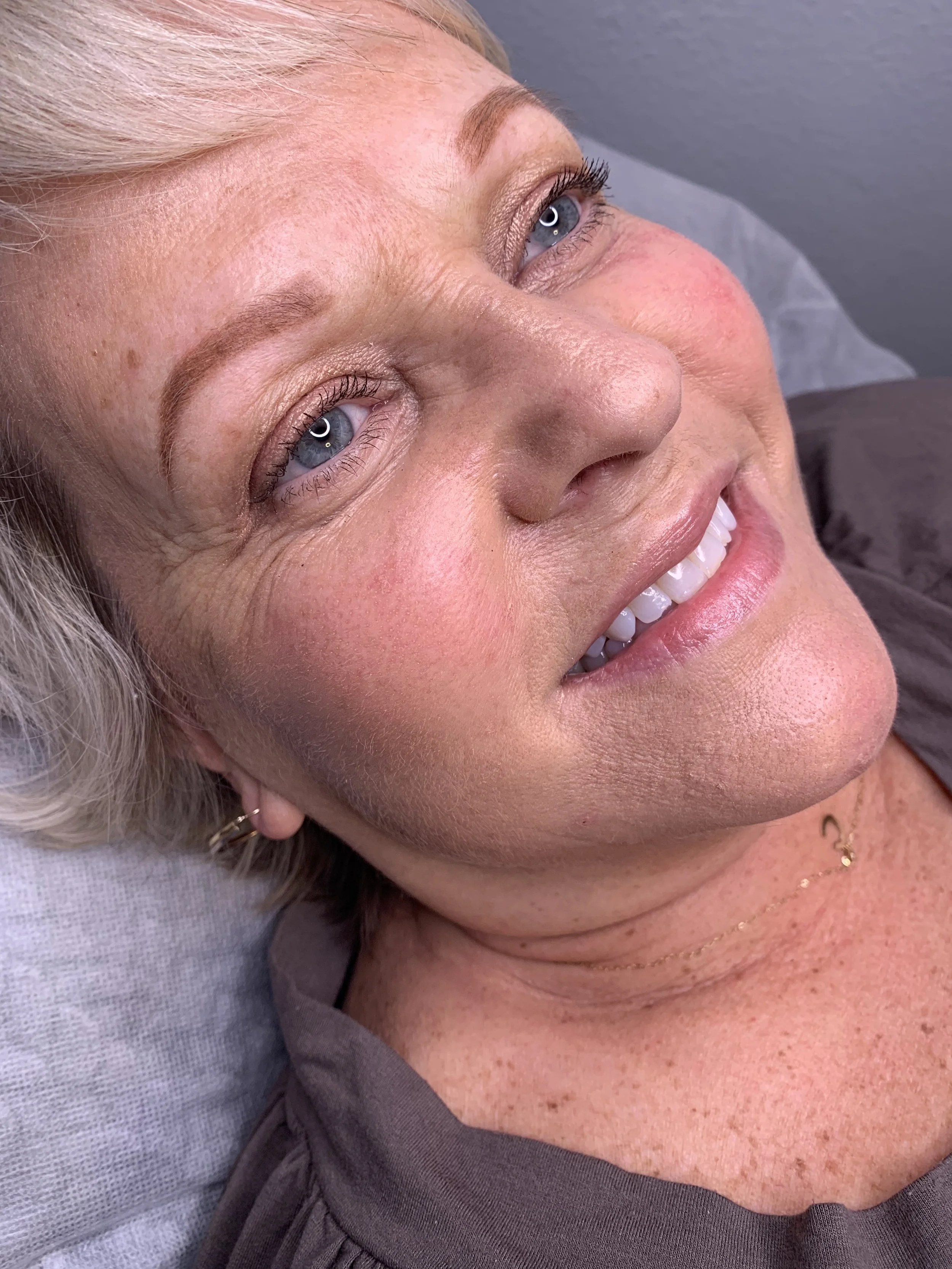 Close-up of a woman lying down, showing her smiling face, blue eyes, blonde hair, and clear skin.