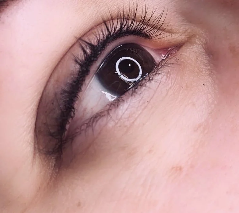Close-up of a human eye showing detailed eyelashes, eyelid, and skin texture, with a reflection of a ring light in the eye.