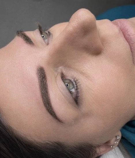 Close-up of a woman's face with well-defined eyebrows and light eye makeup, lying on her side.