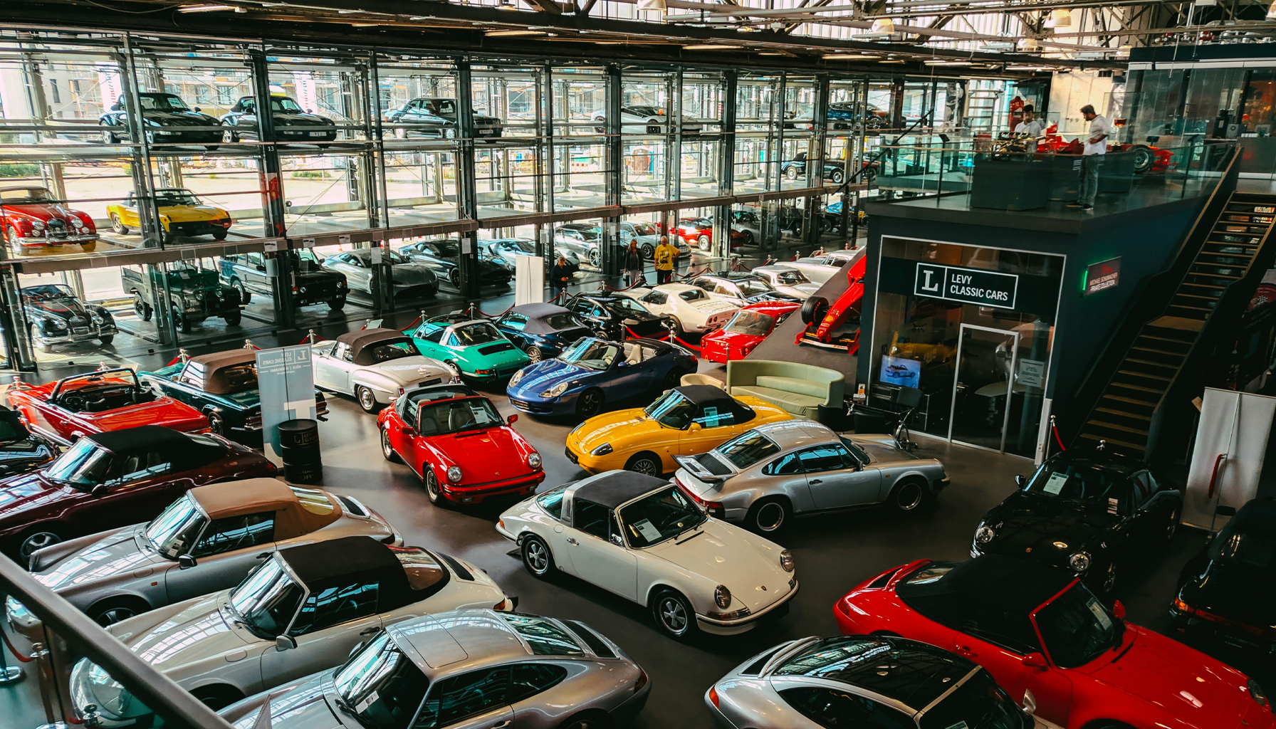 Interior view of a car showroom displaying a collection of classic and vintage cars, with multiple levels and large glass walls.