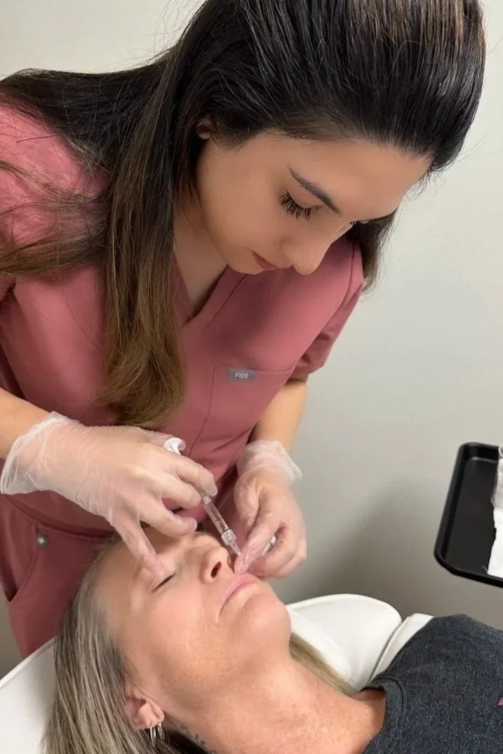 Medical professional administering a cosmetic injection to a woman lying down in a clinic setting.