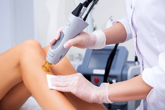 A medical professional performing a laser treatment on a patient's knee, wearing gloves and using a handheld device.