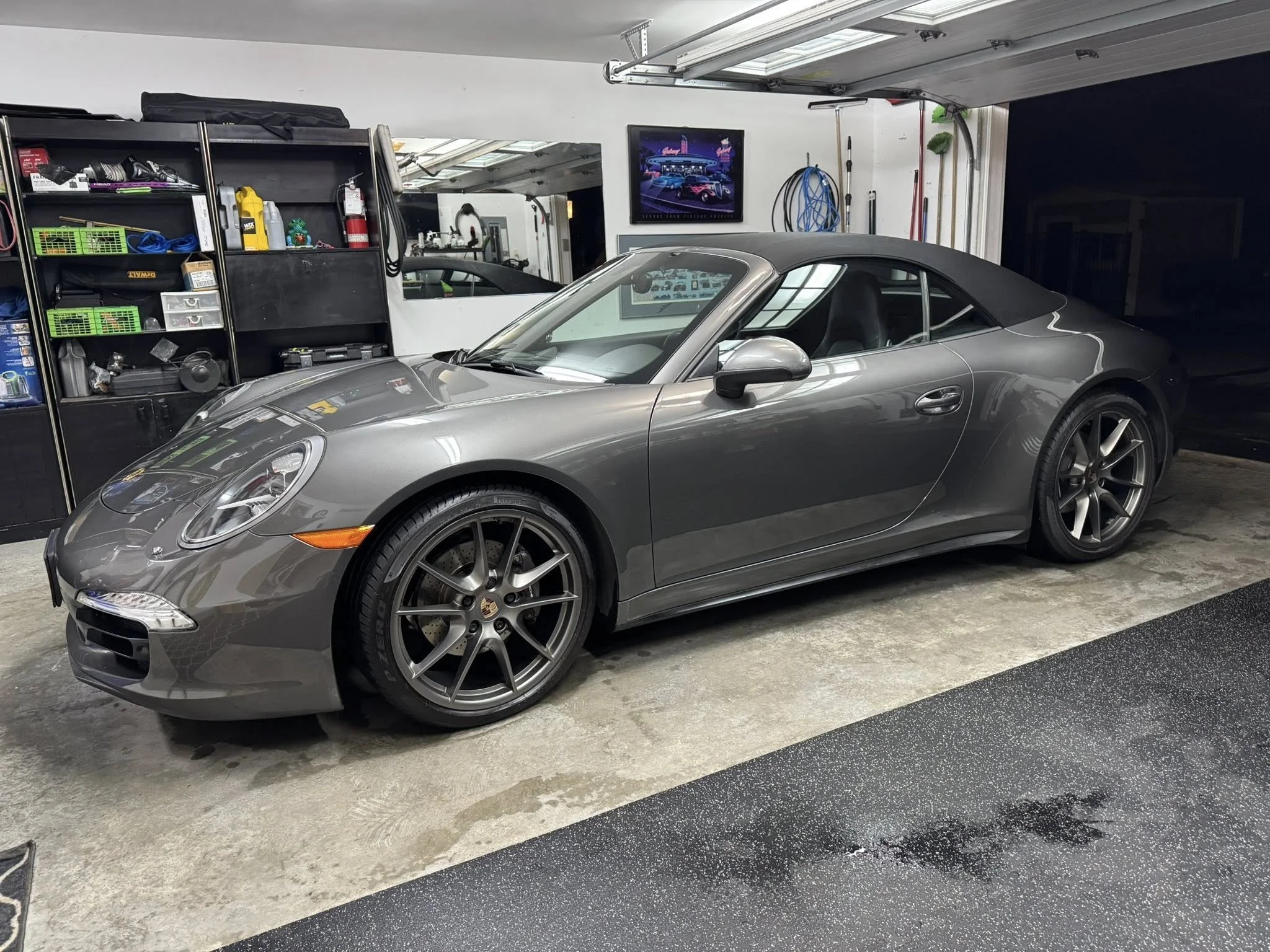 Gray Porsche convertible sports car freshly detailed parked inside a garage, with black wheels and a black soft top roof.