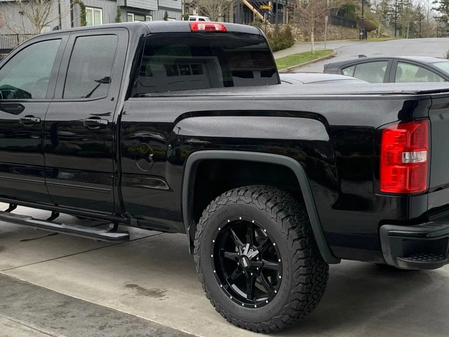 A clean black pickup truck parked in a driveway with large off-road tires and black custom rims.