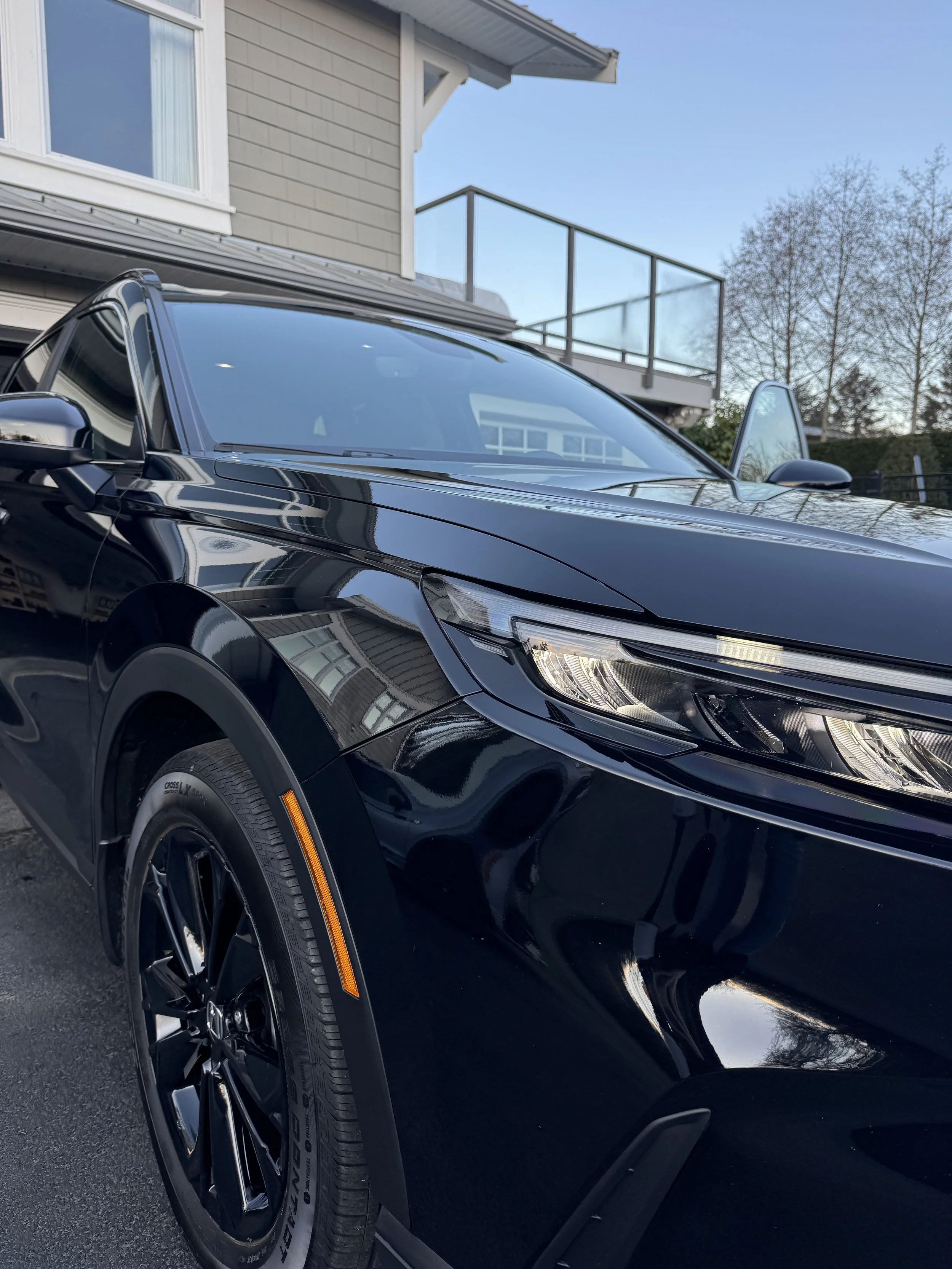 Close-up view of a shiny black sports car parked in front of a residential building with a balcony and a clear blue sky.