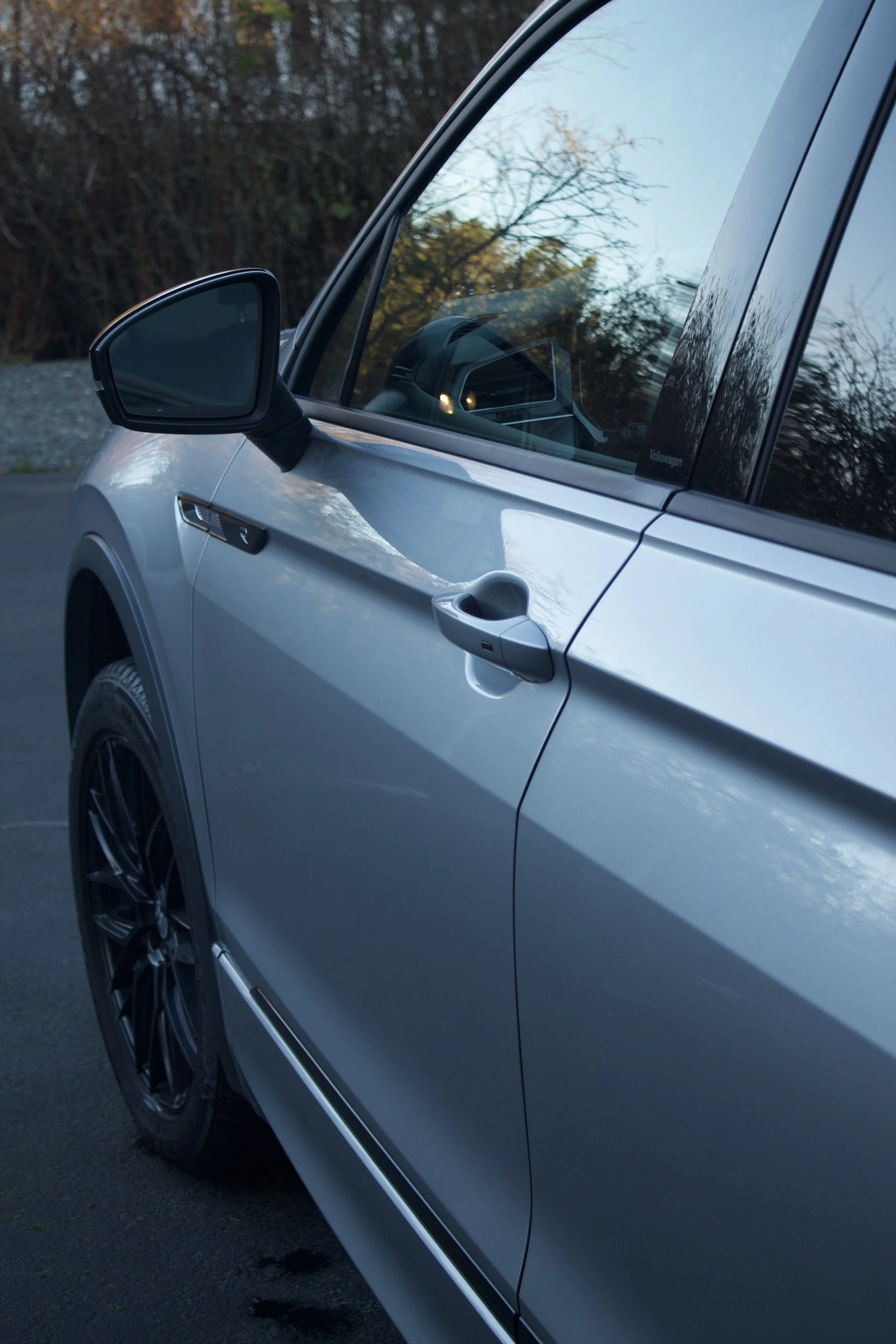 Close-up of a freshly washed silver car parked outdoors, showing the front left side, including the side mirror, door handle, wheel, and part of the window.