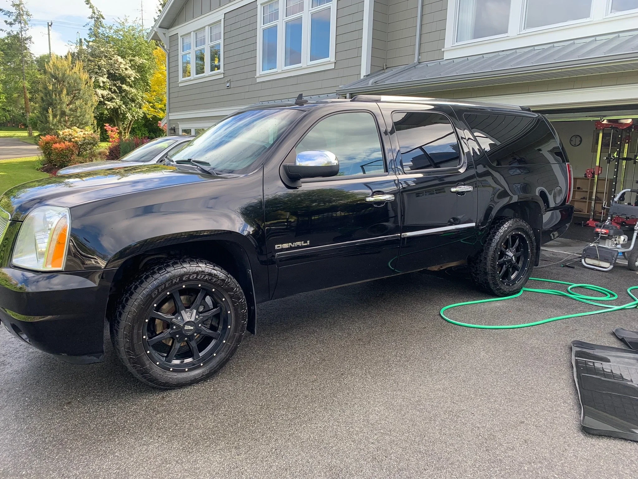 A black GMC Yukon Denali parked on a driveway next to a house, being washed with water and soap.