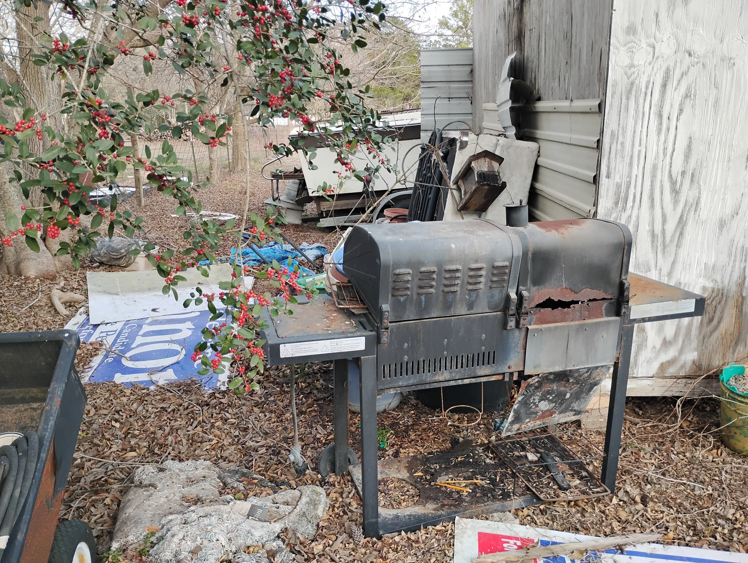 A rusty old grill outside, surrounded by other junk and trash.