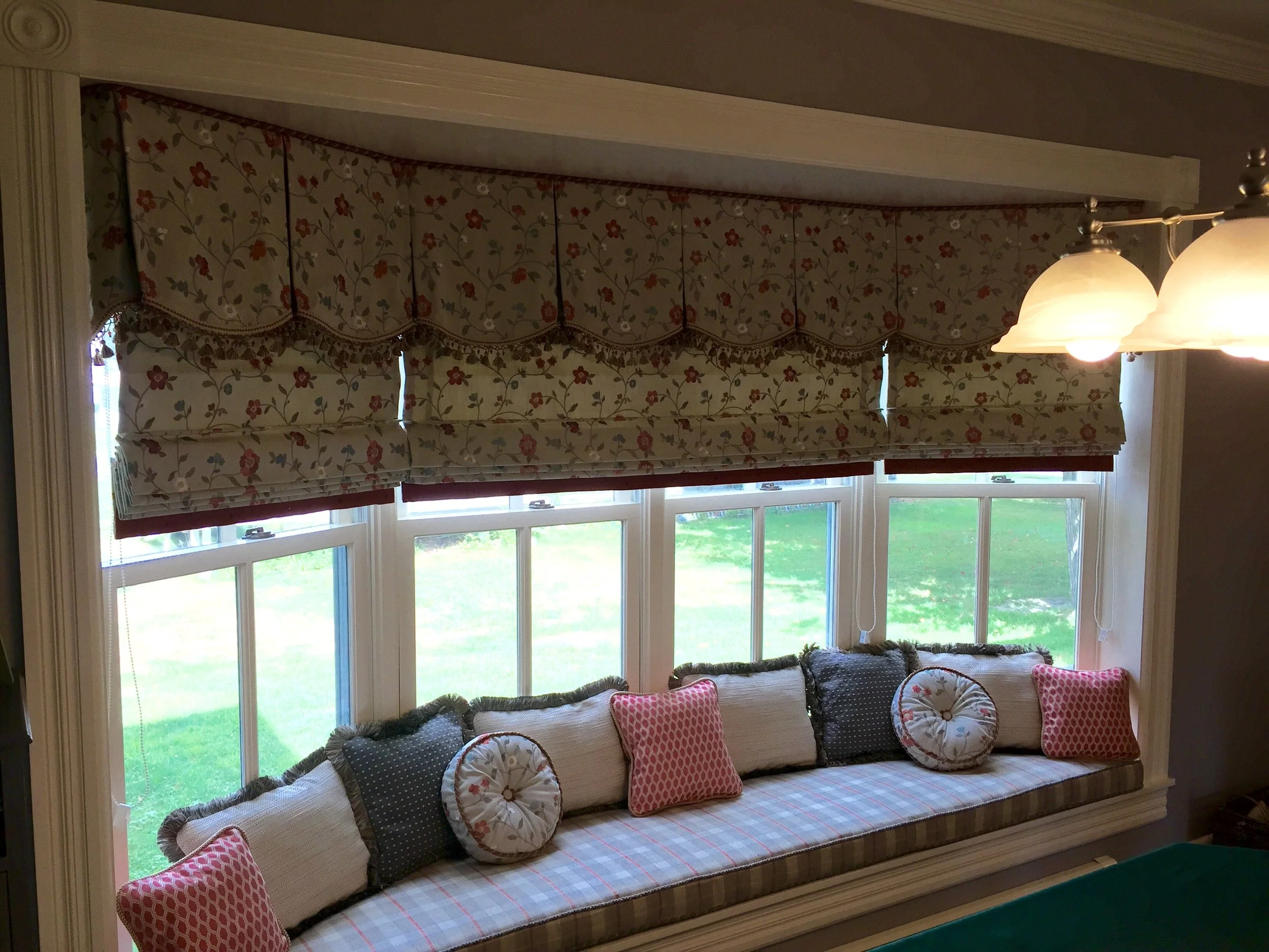 A window seat with various decorative pillows and floral window treatments all made in our workroom at Factory Direct Window Treatments.
