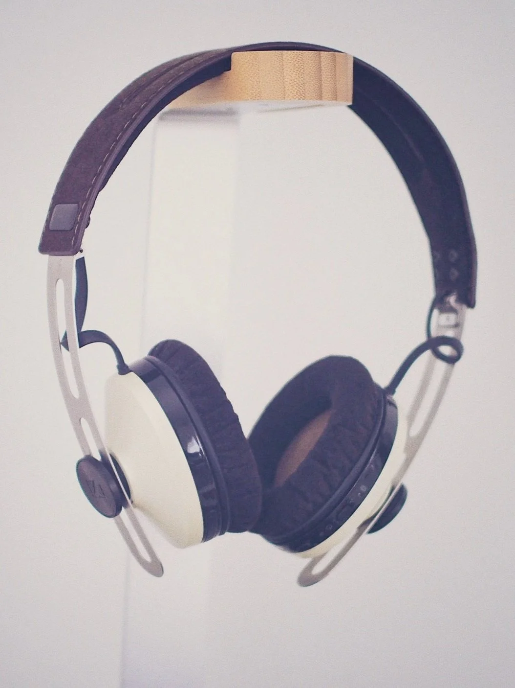 Over-ear headphones with white ear cups, brown headband, and black padding on the ear cushions, hanging in front of a plain light-colored background.