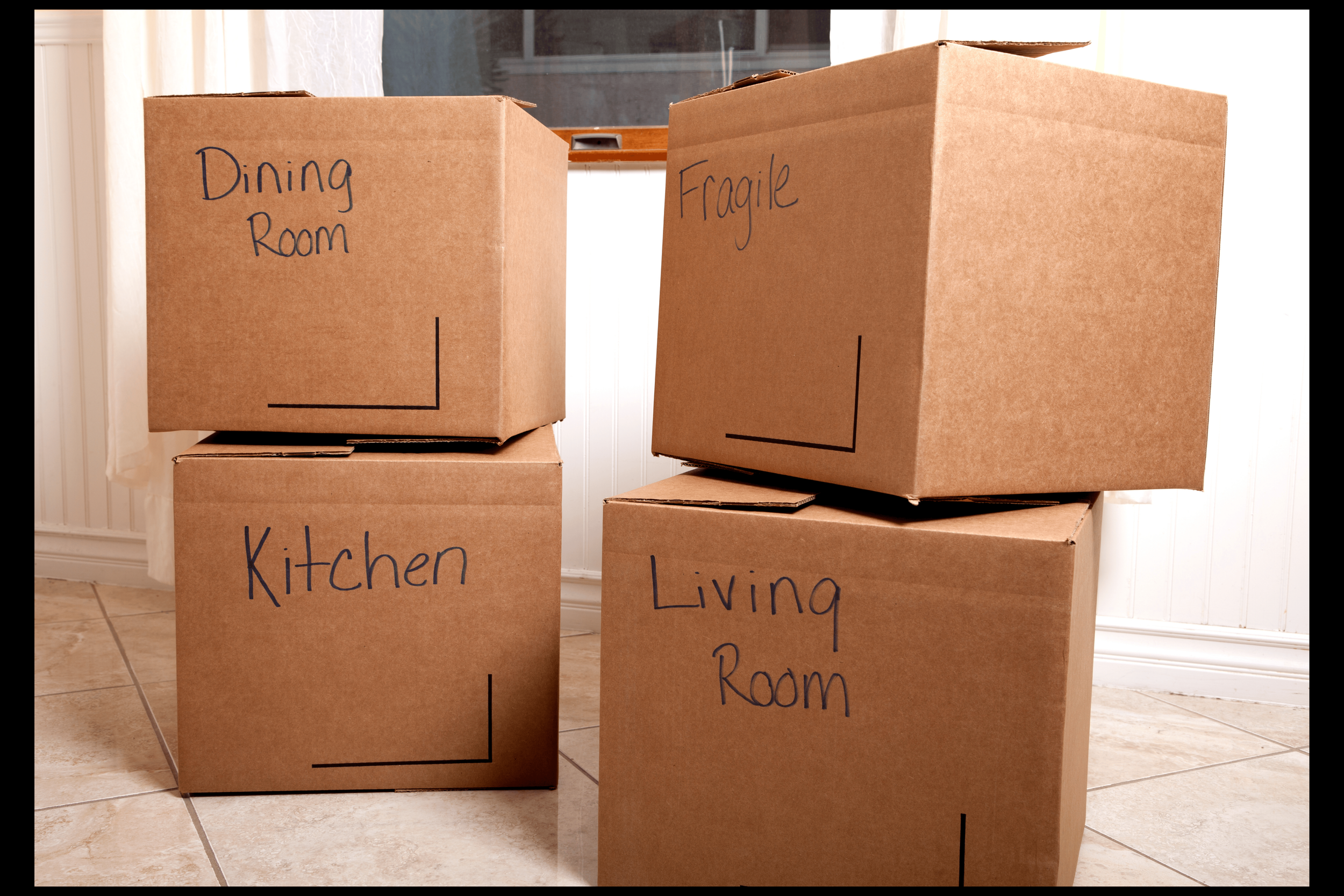 A truck with a yellow sign, parked next to a black Mercedes-Benz van, has its back open revealing washing machines and water cooler bottles inside. The truck is on an urban street near a waterfront with high-rise buildings in the background.