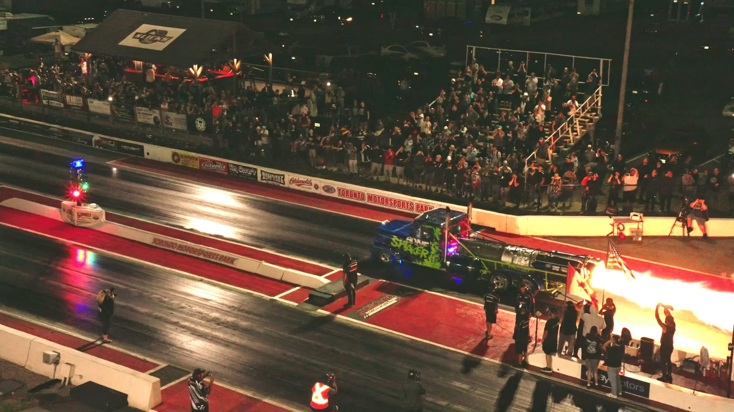 Drag cars launching at night in front of a full grandstand