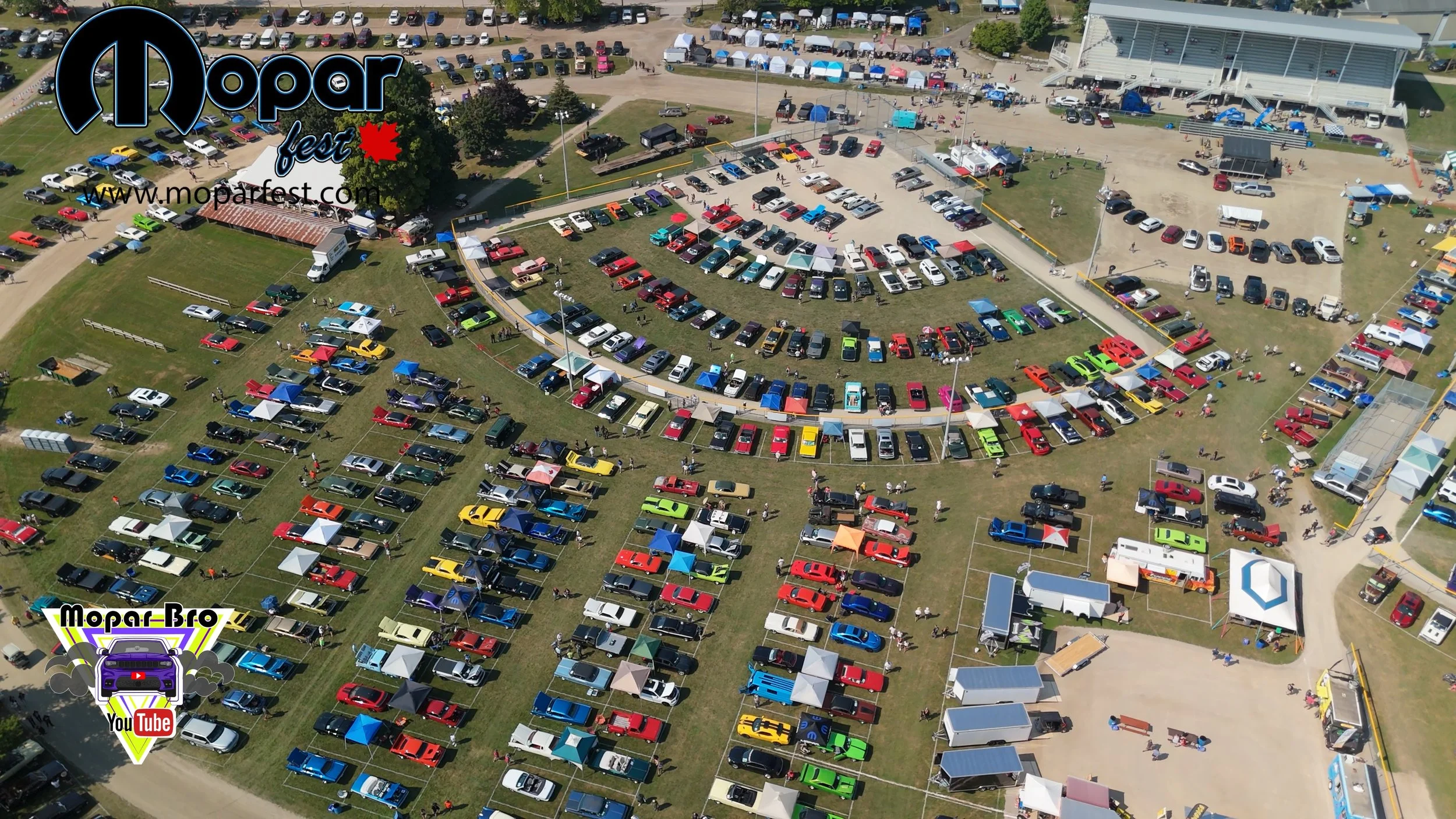 Aerial view of Mopar Fest at a large outdoor venue with numerous cars, tents, and vendor booths, featuring a curved zone of parked vehicles, a stage area, and various event activities.