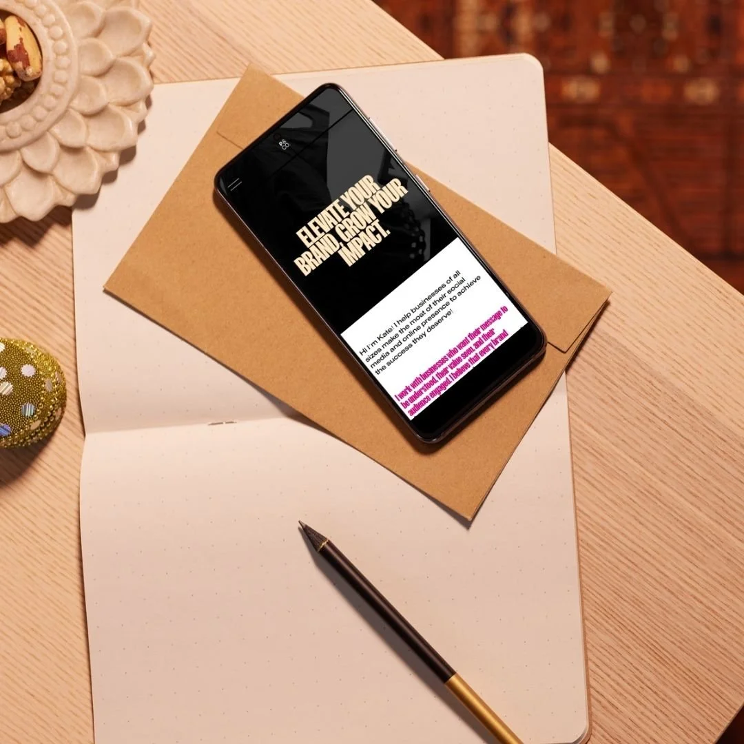 Smartphone on top of a brown envelope and white paper, pen beside it on a wooden desk, part of decorative objects visible.