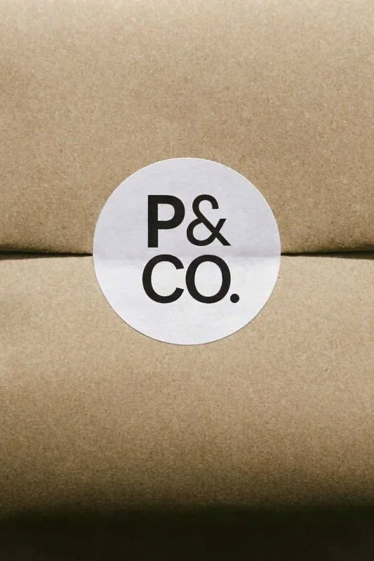 A white circular sticker with bold black text reading "P & Co." on a plain brown cardboard surface.