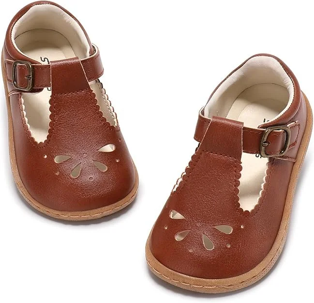 Brown toddler Mary Jane shoes with a scalloped T strap, pedal cut outs and a rounded wide toe.