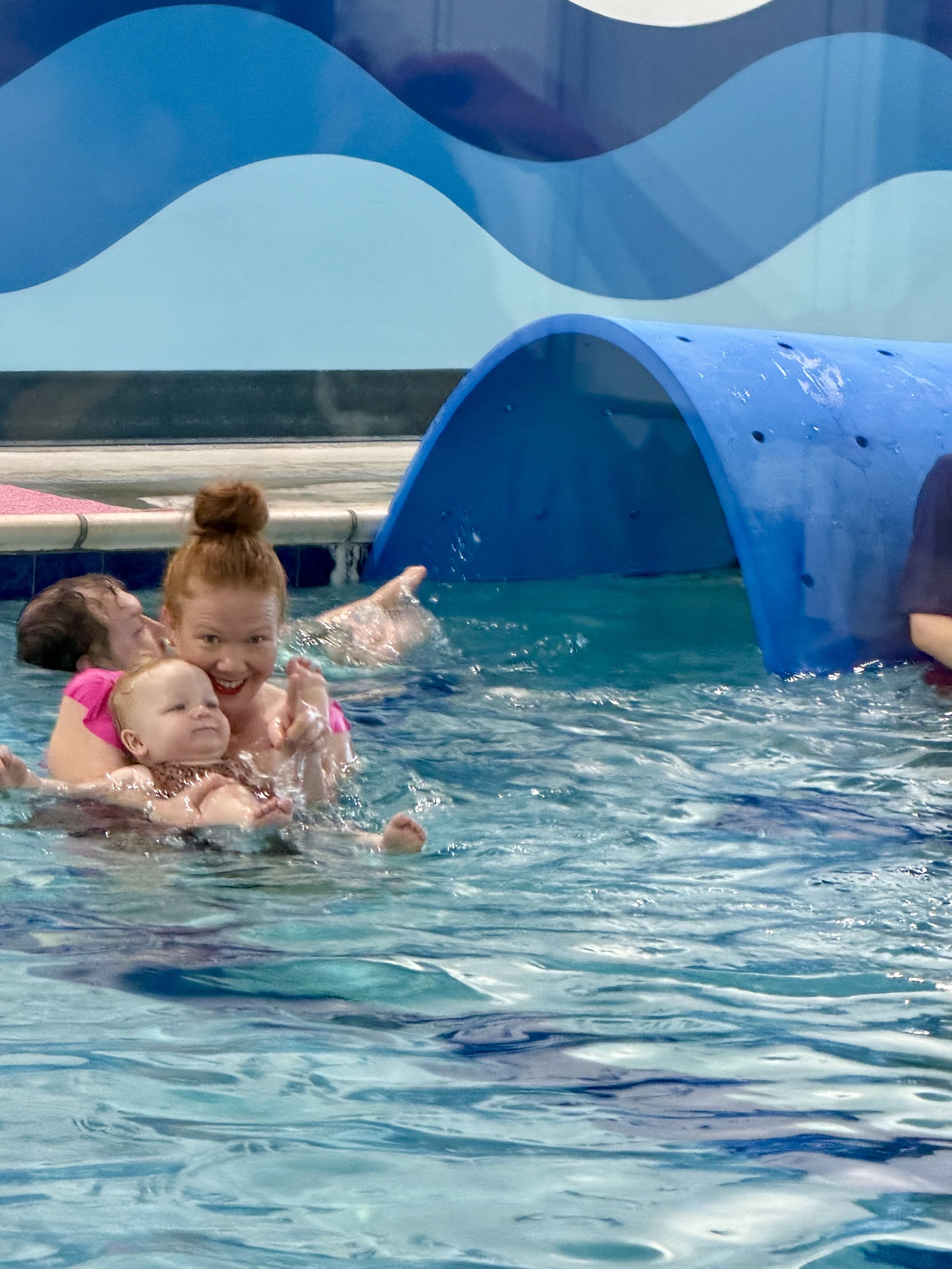 A mother and her toddler daughter in a swimming pool during a parent-and-baby swim class.