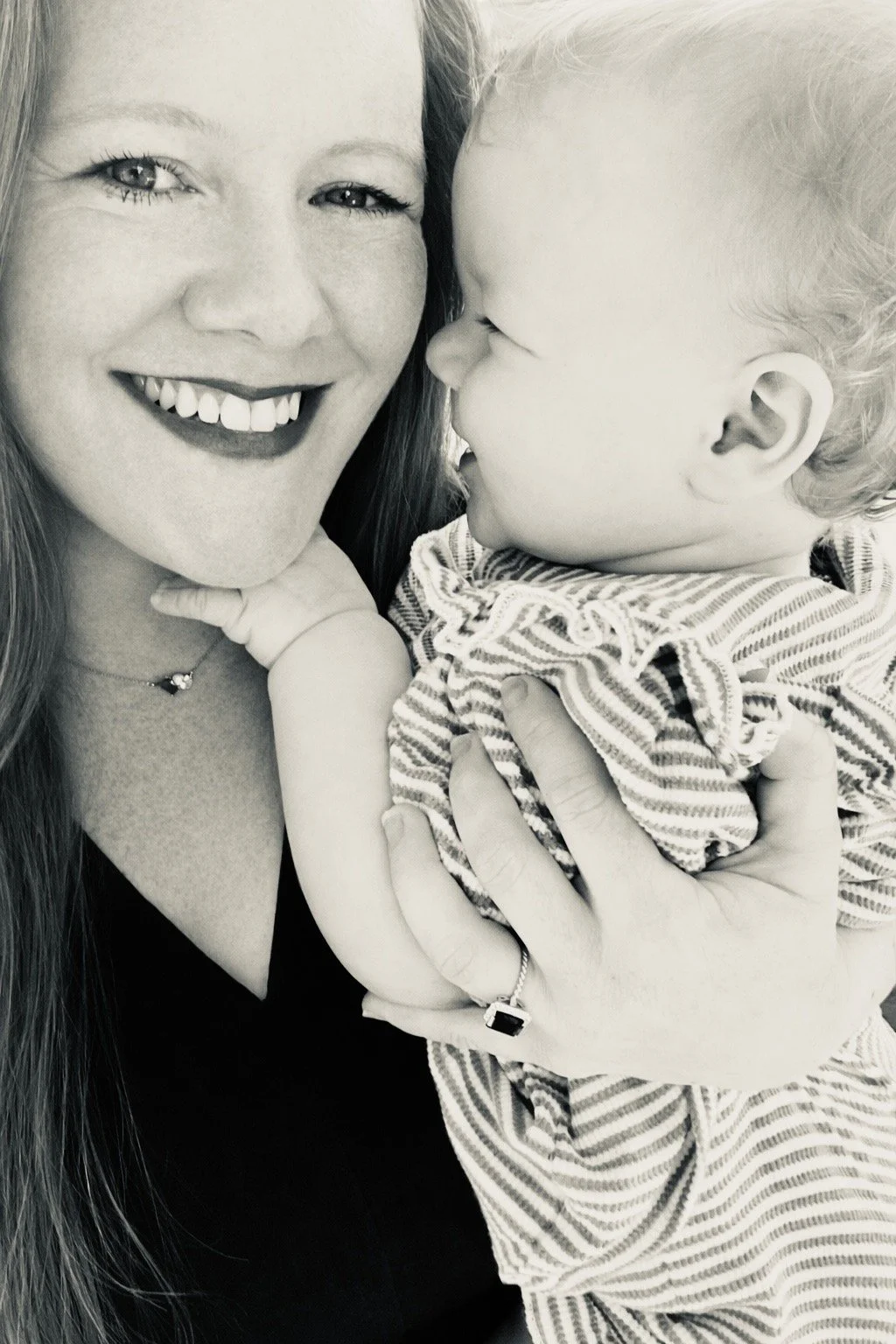 A woman holding a young child in her arms, smiling happily with their faces close together in black and white.
