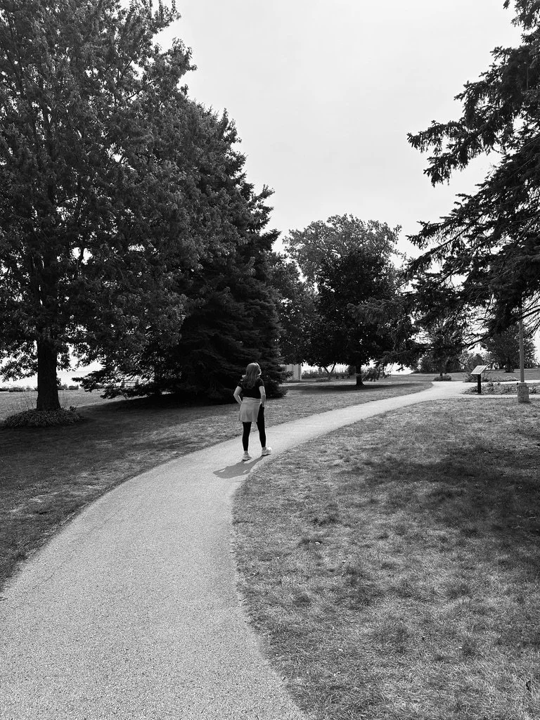 Black and white photo of a pregnant single mother walking on a winding path near Lake Michigan during a healing journey after trauma.