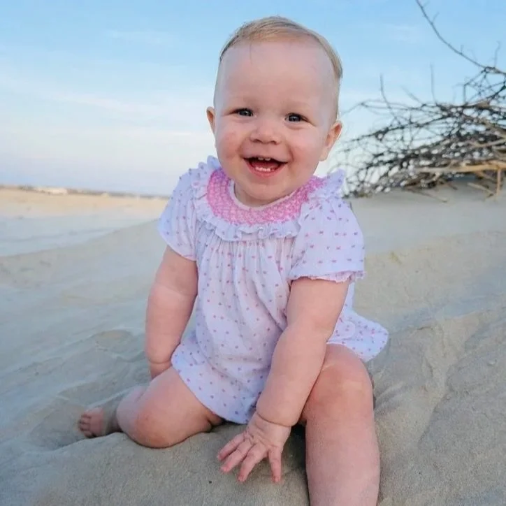 Smiling toddler girl sitting on the beach in Corpus Christi, Texas during a family motherhood and healing lifestyle blog.