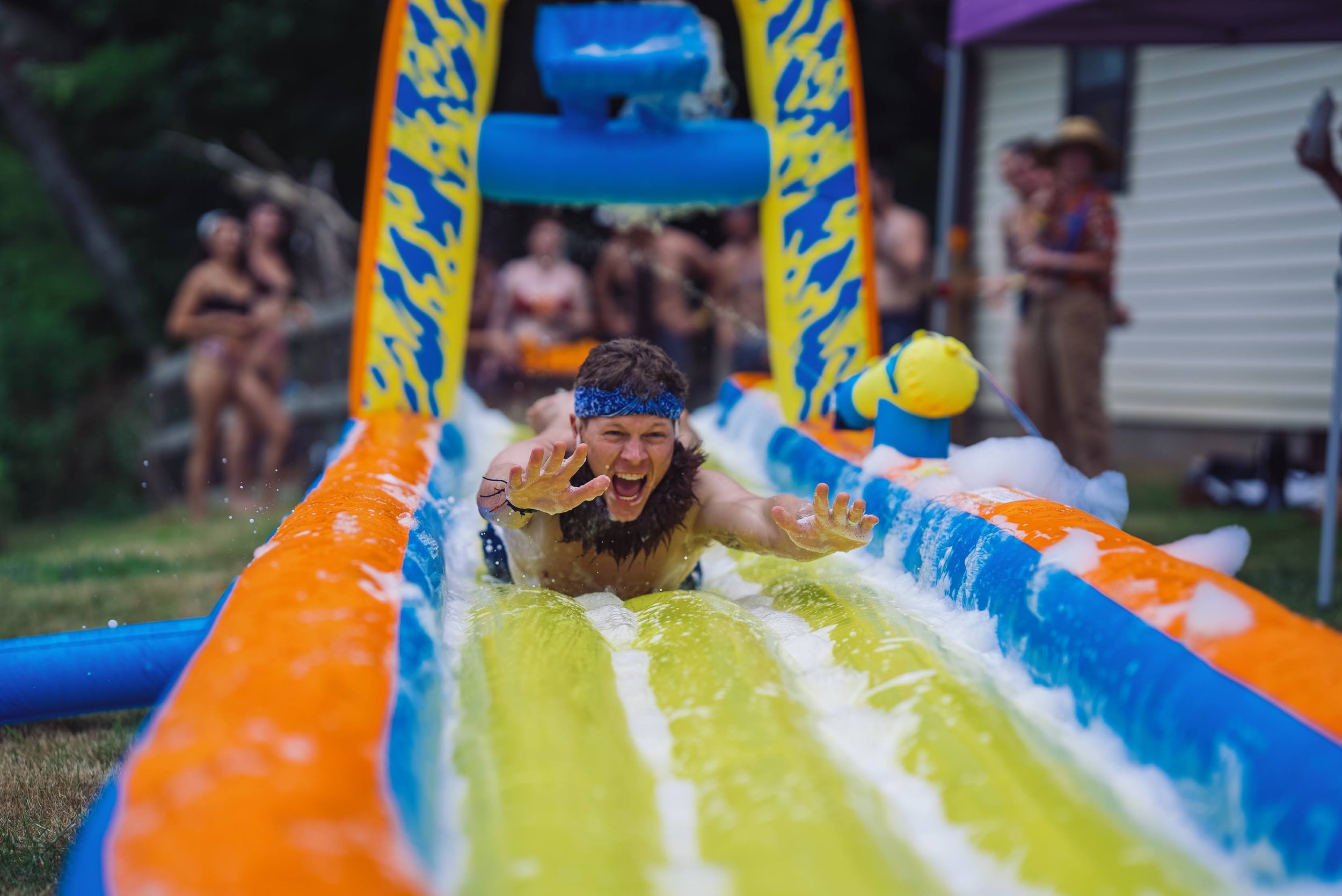 A man wearing a blue bandana slides down an inflatable water slide during community games and creative workshops during Churning Man arts festival in North Carolina