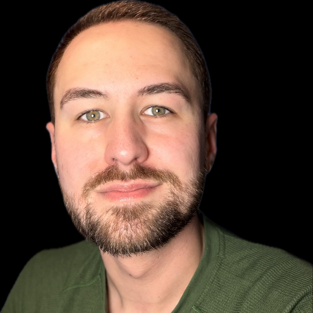 Close-up of a young man with light skin, short brown hair, green eyes, and a full beard, wearing a green shirt, against a black background.