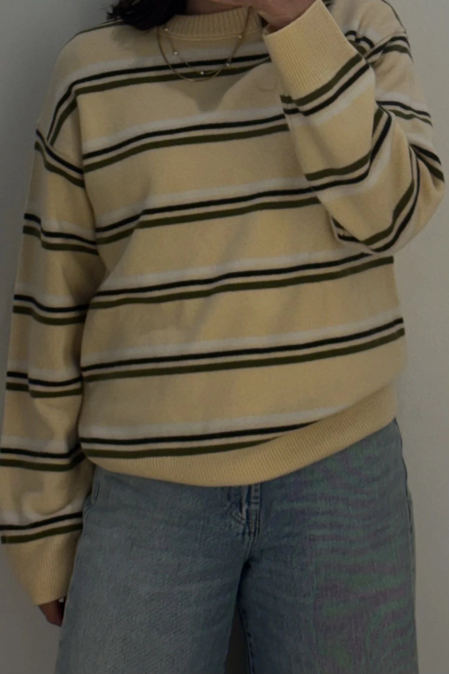 Person wearing a yellow and black striped sweater and light blue jeans, taking a mirror selfie.
