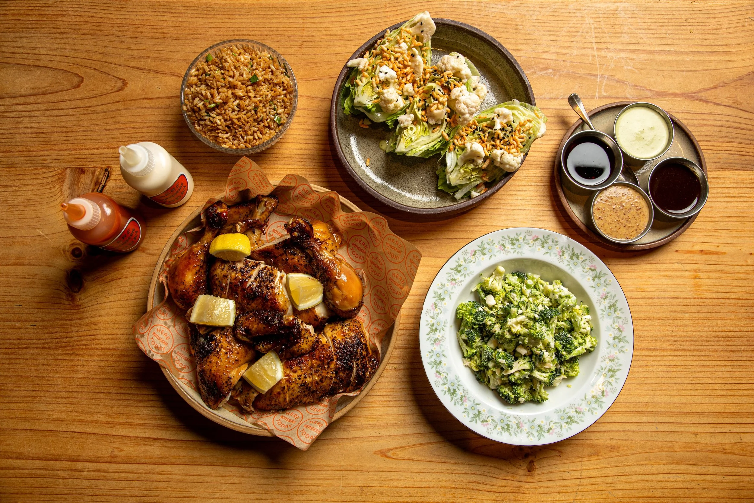 Aerial view of rotisserie chicken, chicken bowl, broccoli salad, iceberg lettuce salad, and sauces