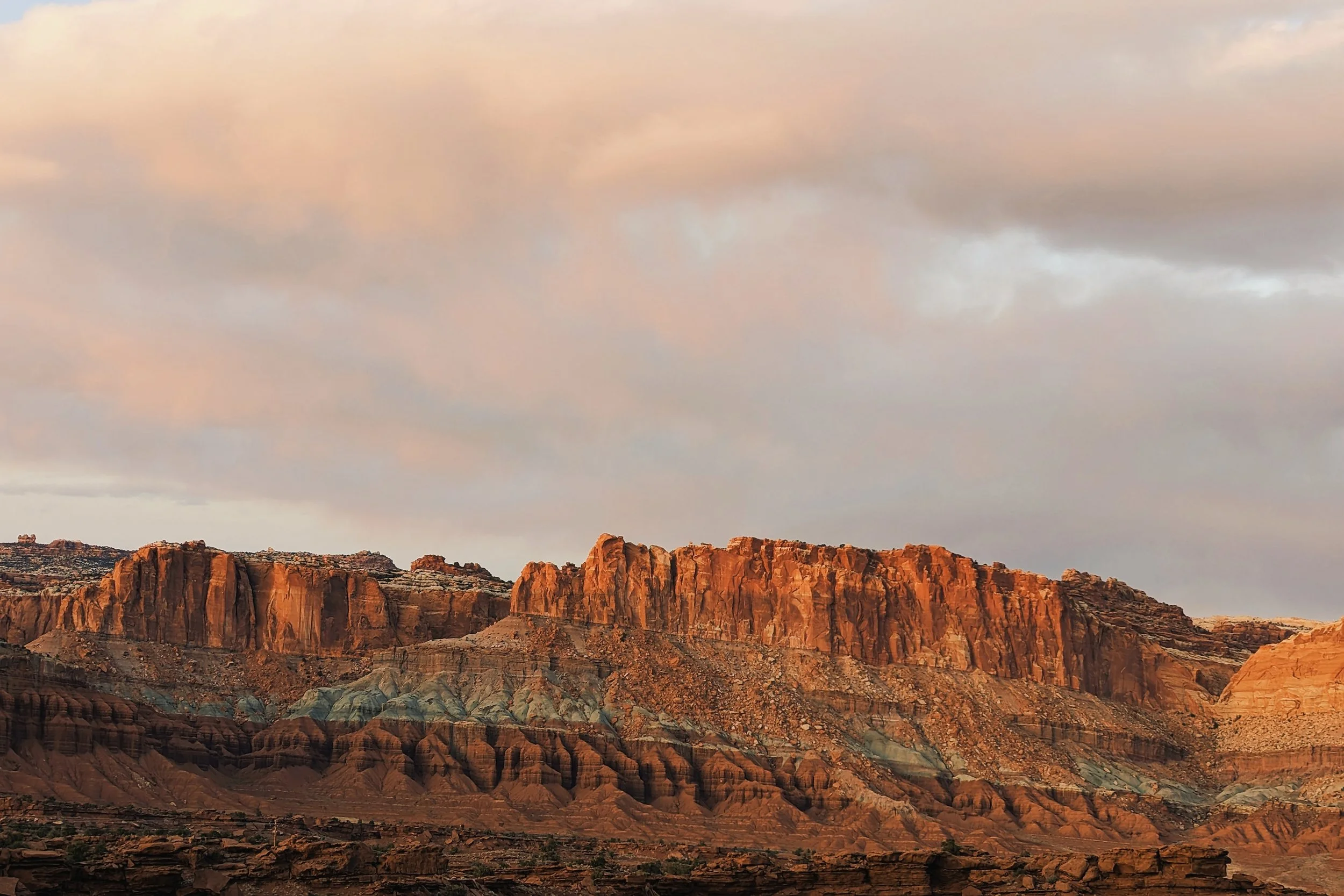Sunset over a rugged desert landscape with colorful cliffs and layered rock formations.