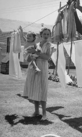 A woman holding a young girl standing outdoors near a clothesline with laundry hanging to dry.