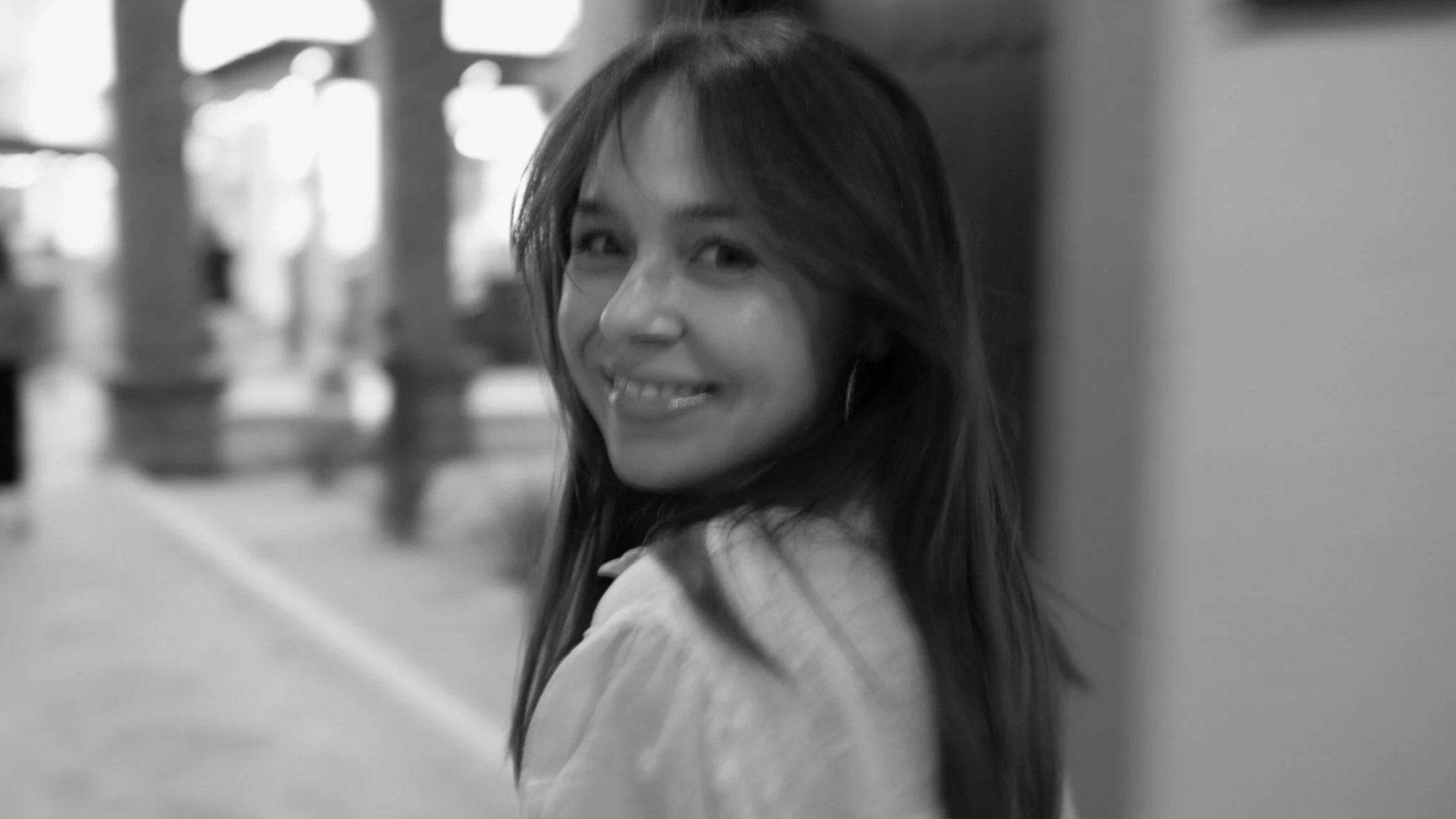 Black and white portrait of a woman looking back and smiling indoors.