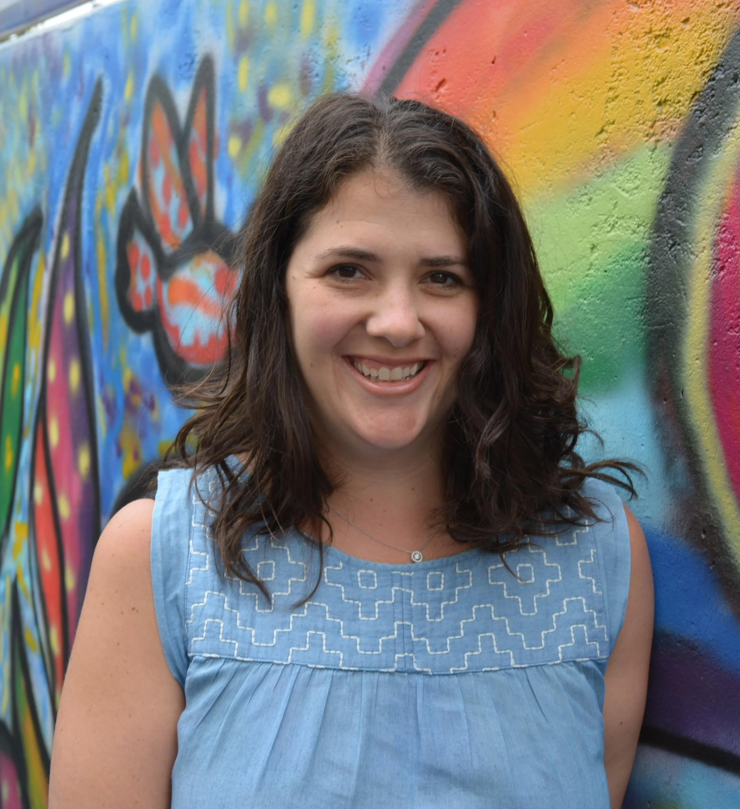 woman smiling in front of colorful graffiti wall