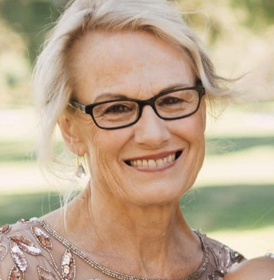 Smiling elderly woman with glasses outdoors, wearing a decorated dress.